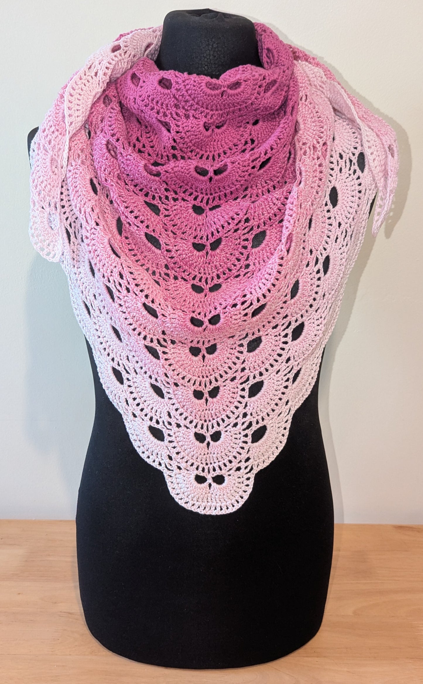 Pink and white crocheted shawl on a black mannequin against a plain background