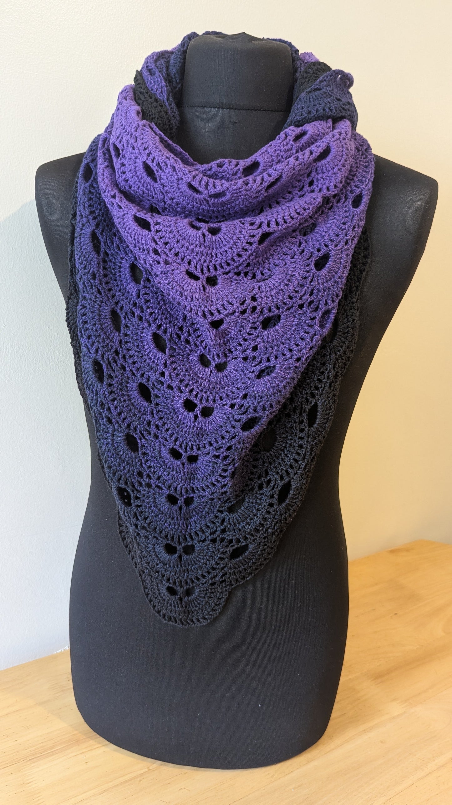 Purple crocheted scarf on a black mannequin against a white background