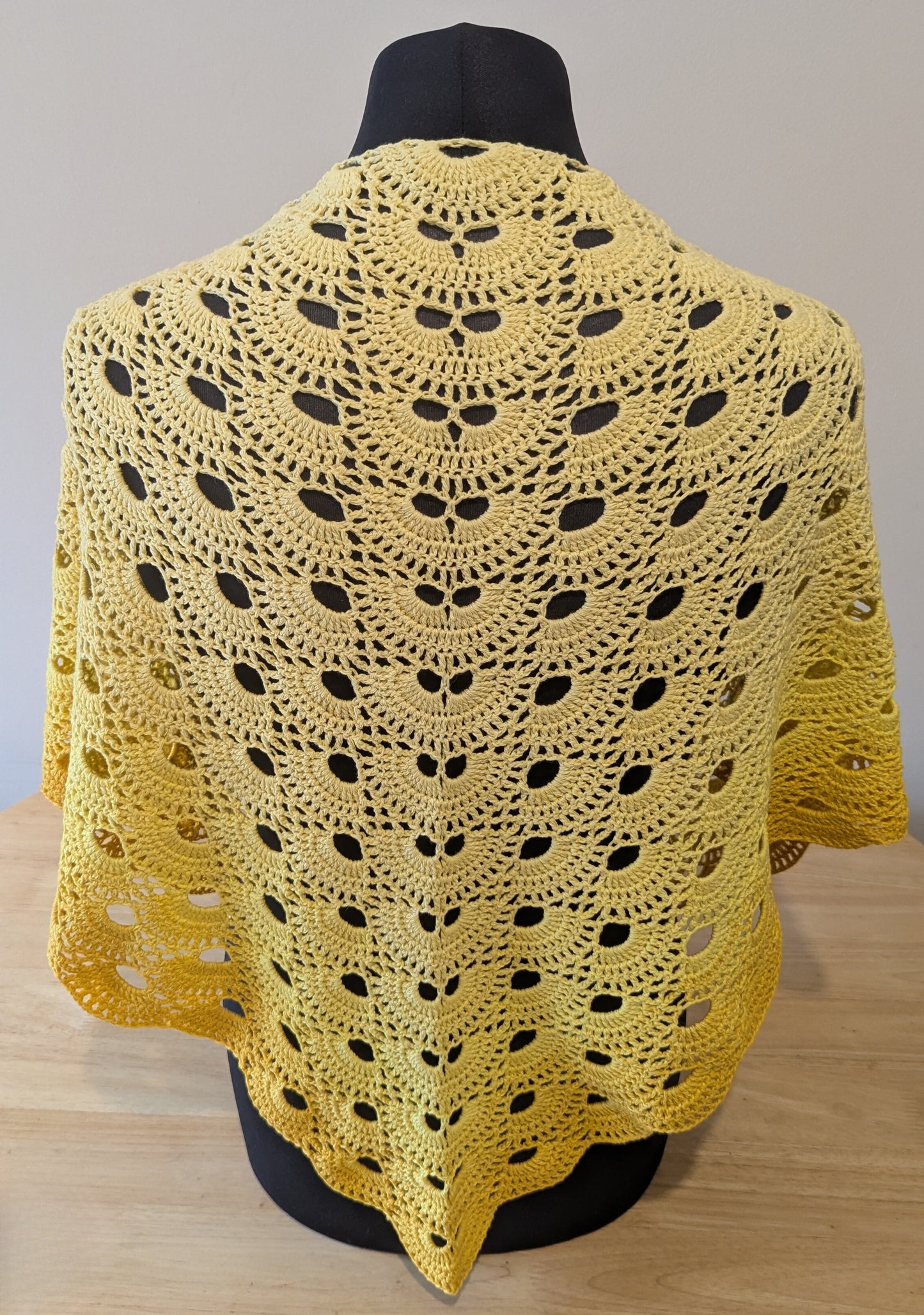 Yellow crocheted shawl on a mannequin against a neutral background