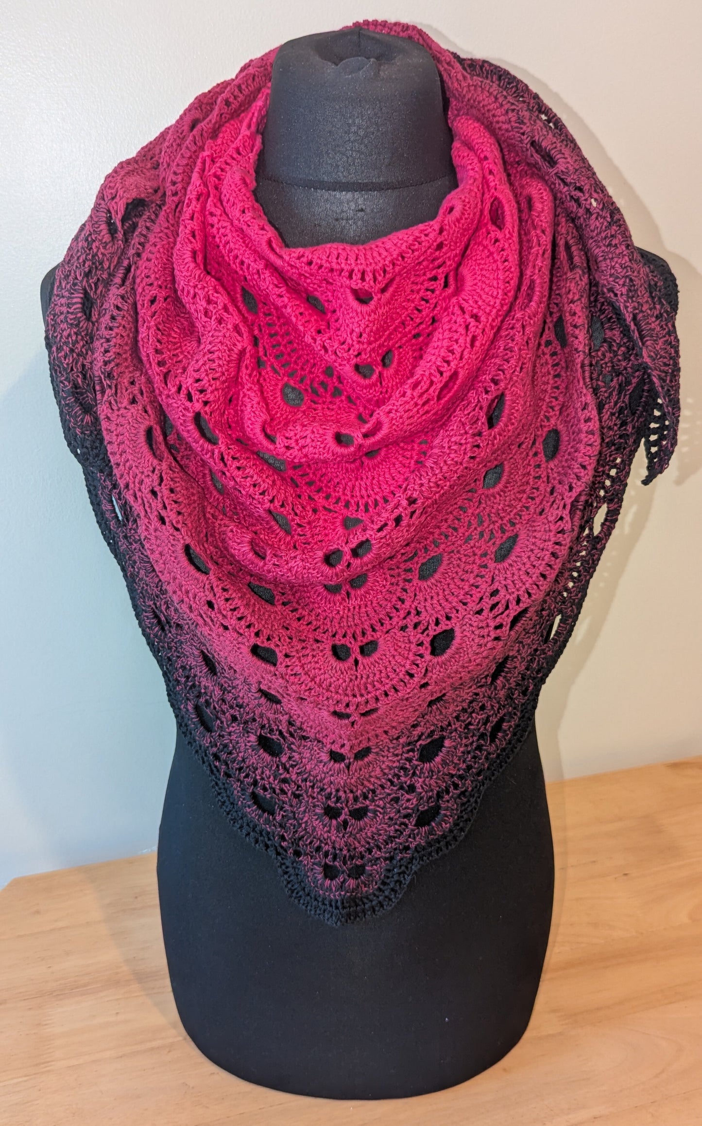 Pink crochet shawl on a black mannequin against a white wall.