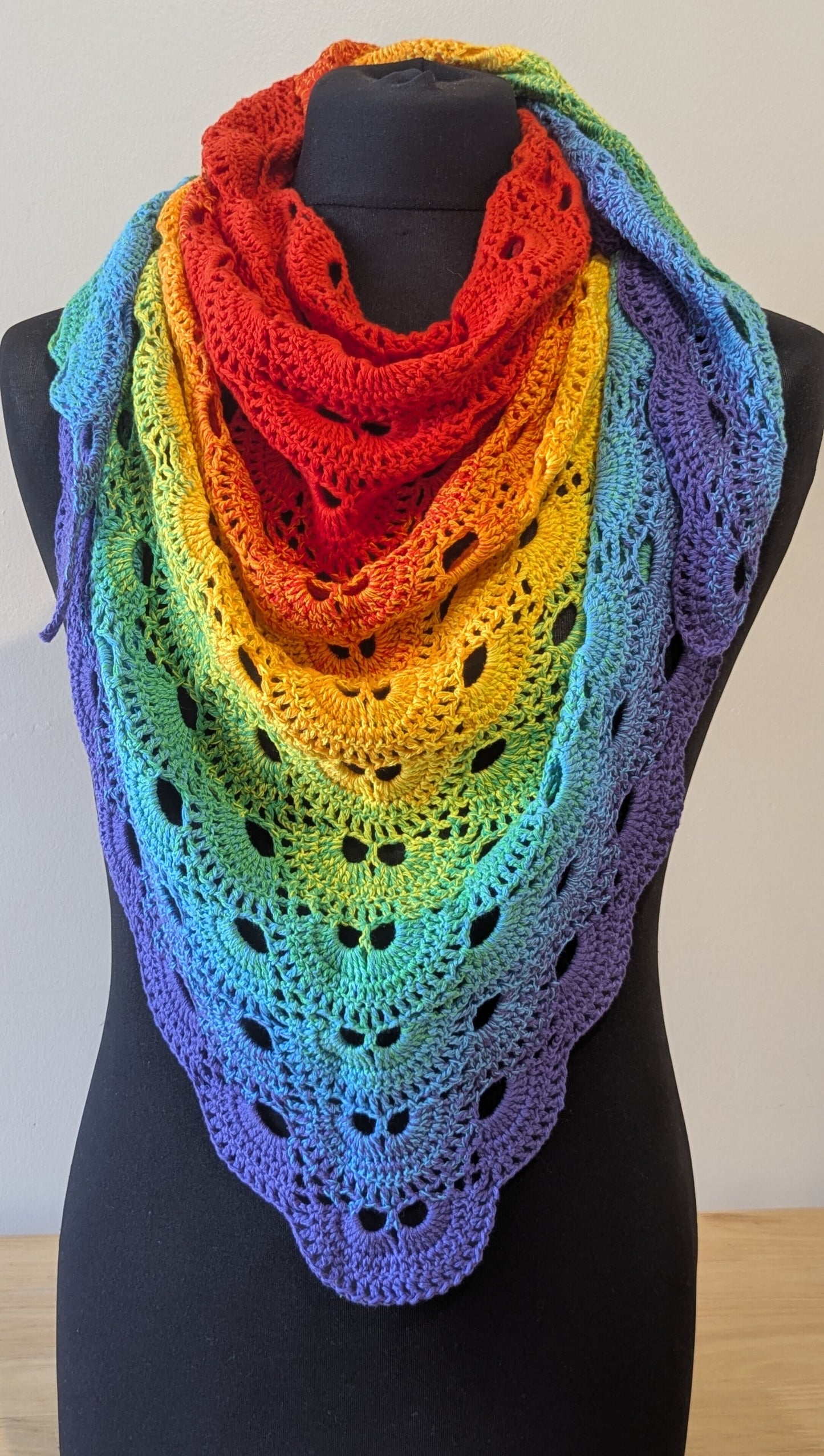 Rainbow-colored crocheted shawl on a mannequin against a plain background