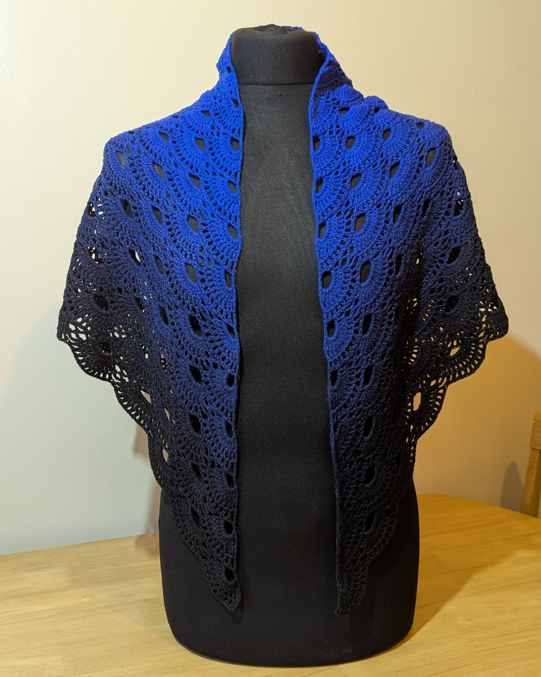 Blue crochet shawl on a black mannequin against a beige wall.