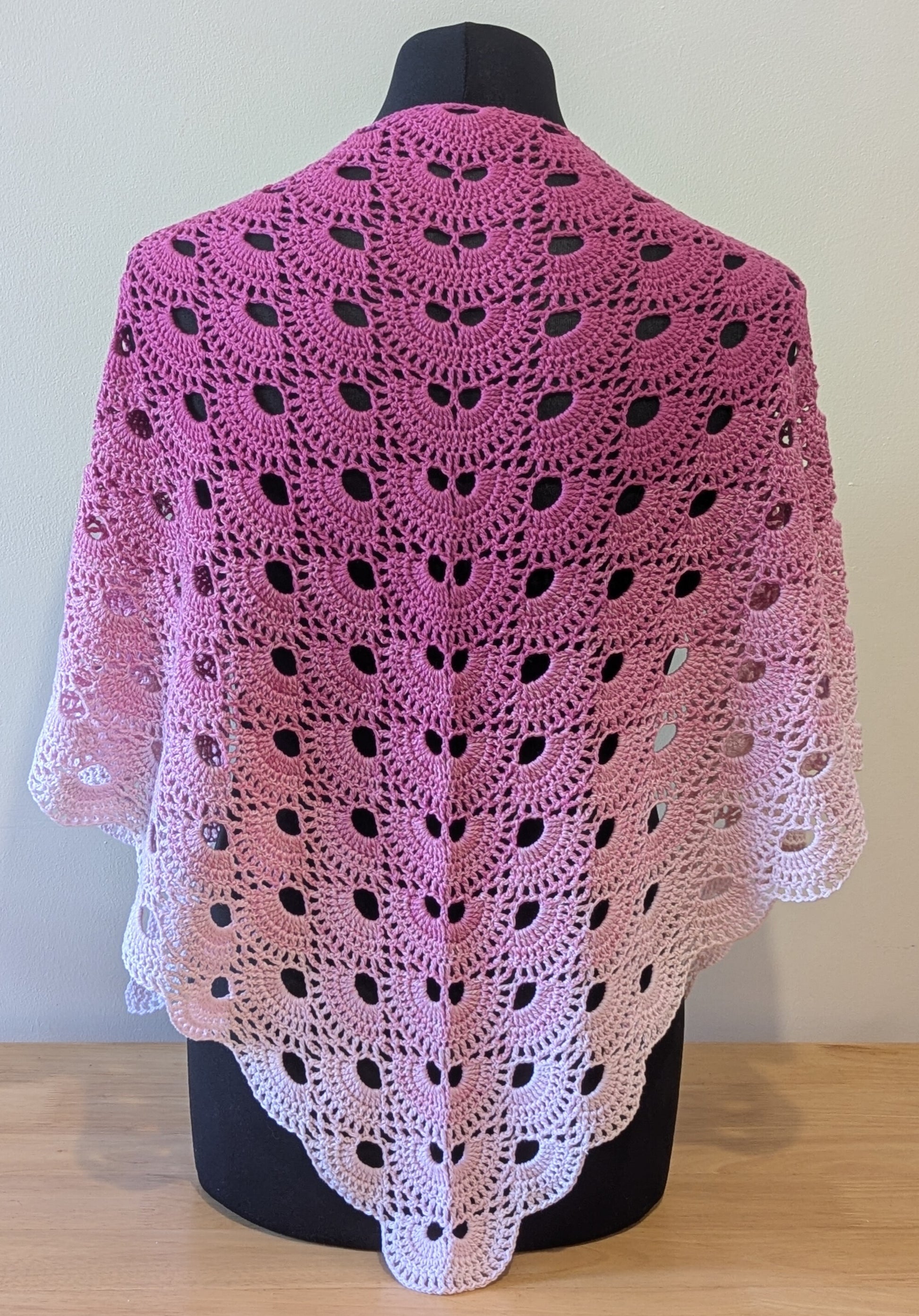 Pink and white crocheted shawl on a mannequin against a plain background