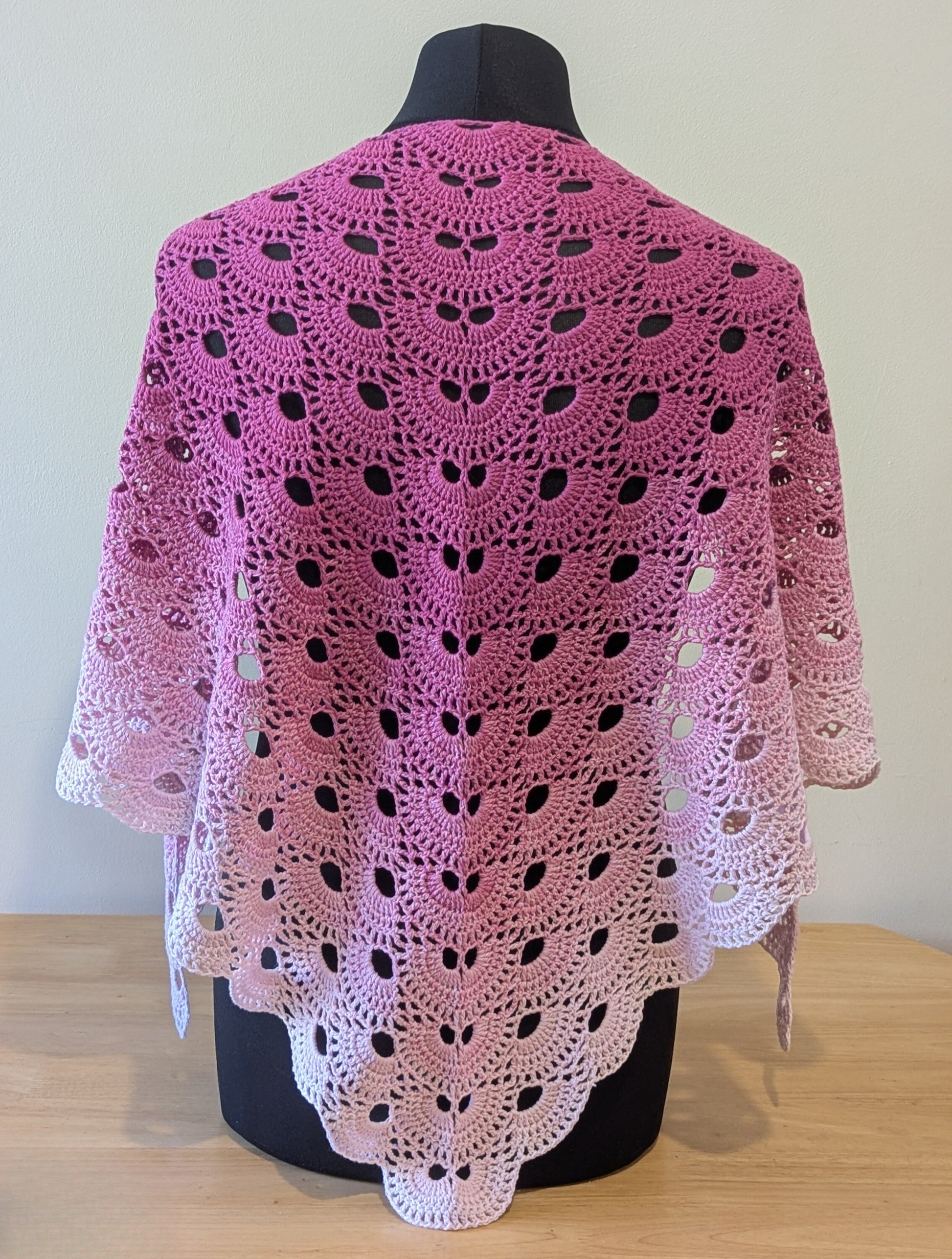 Pink crochet shawl on a mannequin against a plain background
