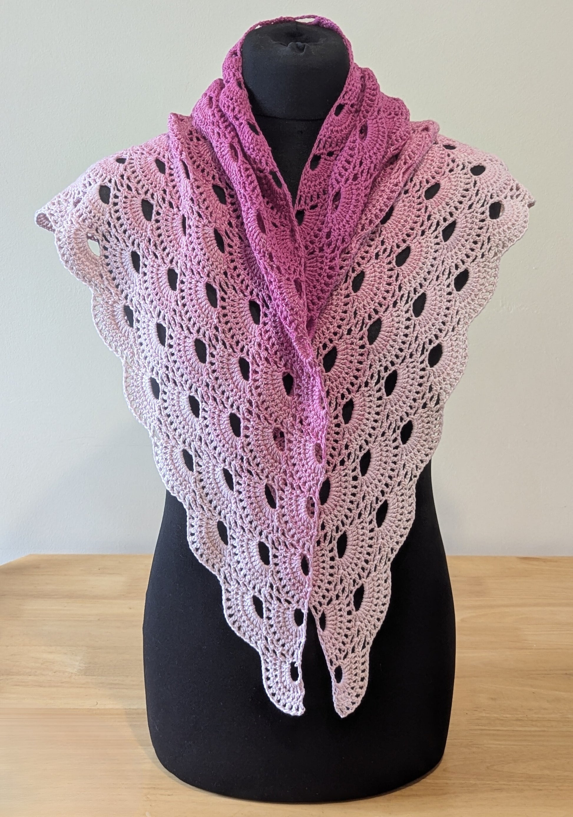 Pink and white crocheted shawl on a mannequin against a plain background