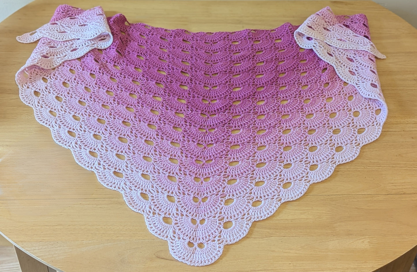 Pink and white crocheted shawl on a wooden surface