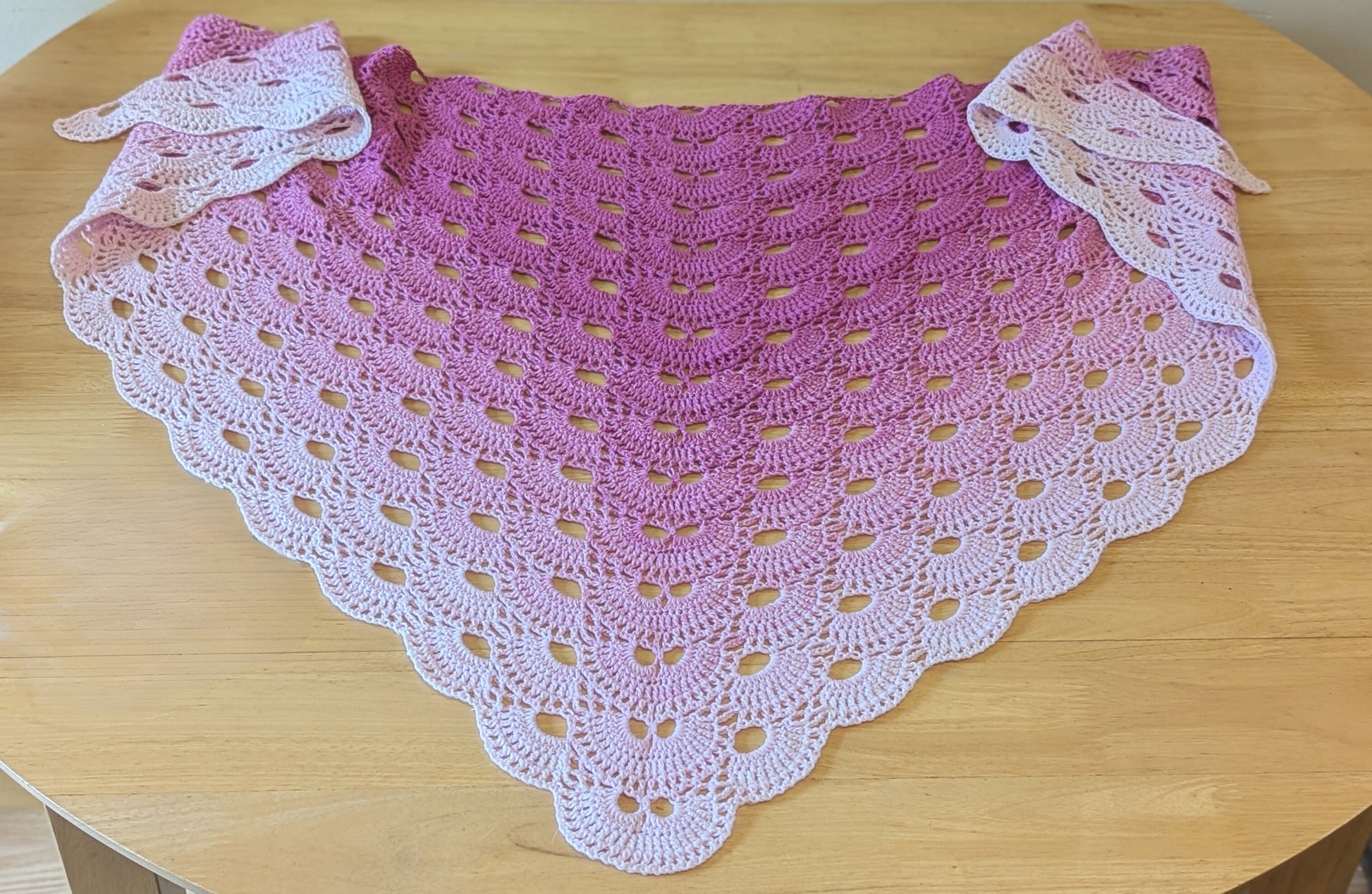 Pink and white crocheted shawl on a wooden surface