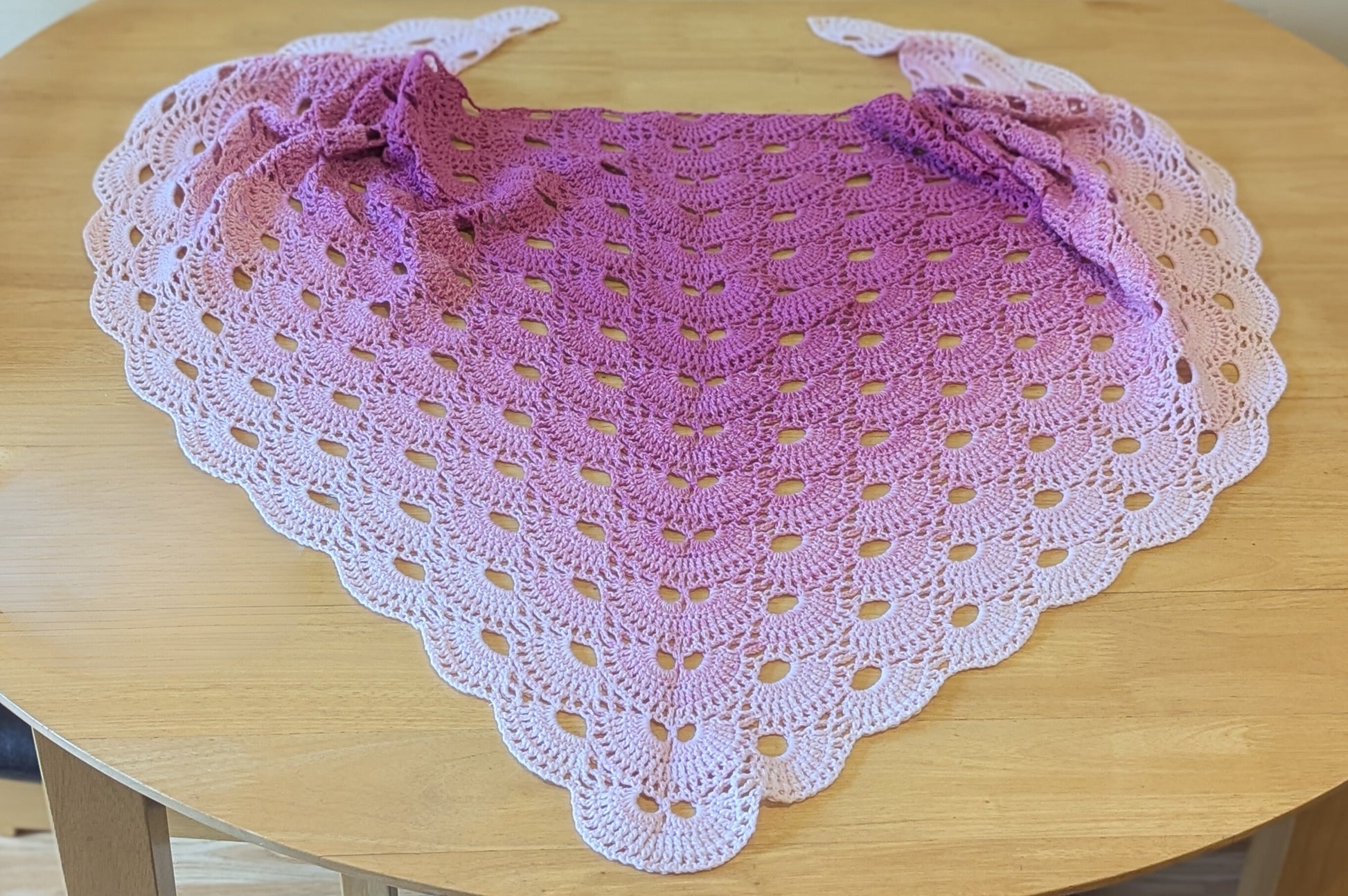 Crocheted shawl with a gradient from pink to light pink on a wooden table.