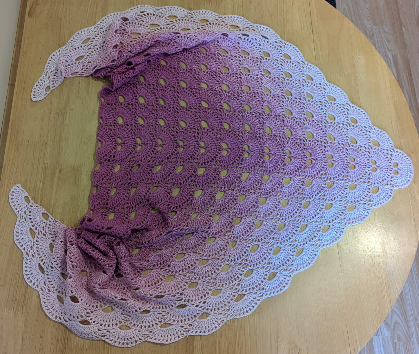 Pastel pink crocheted shawl on a wooden surface