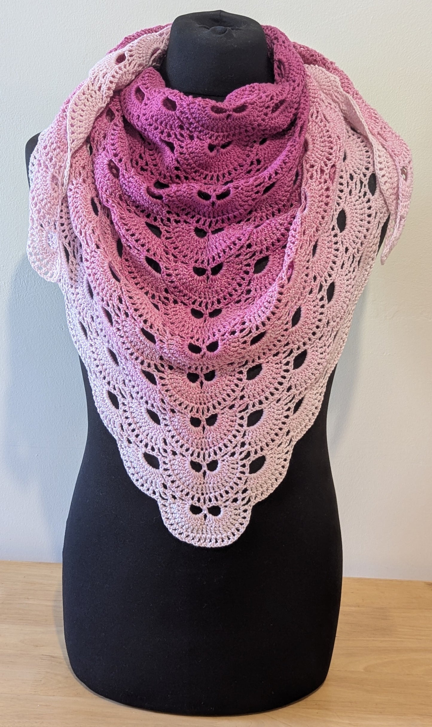 Pink crochet shawl on a black mannequin against a white background