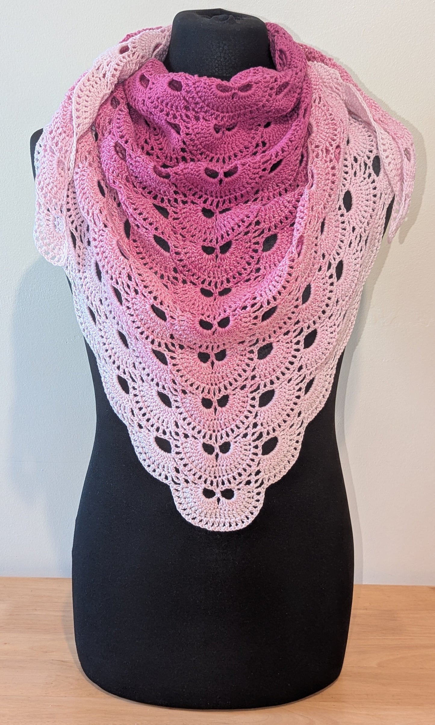 Crocheted shawl with pink gradient on a mannequin against a plain background