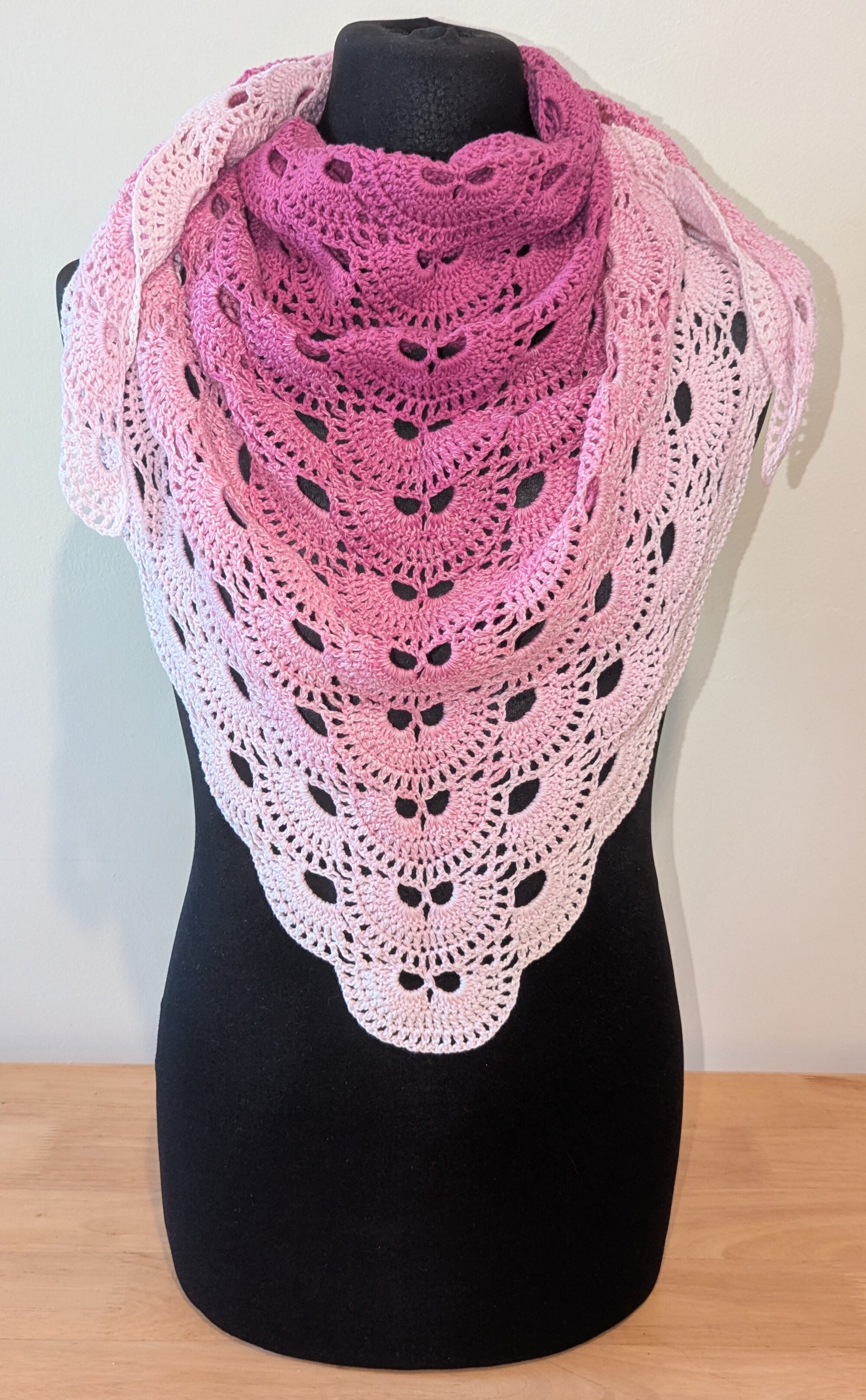 Pink and white crocheted shawl on a black mannequin against a plain background
