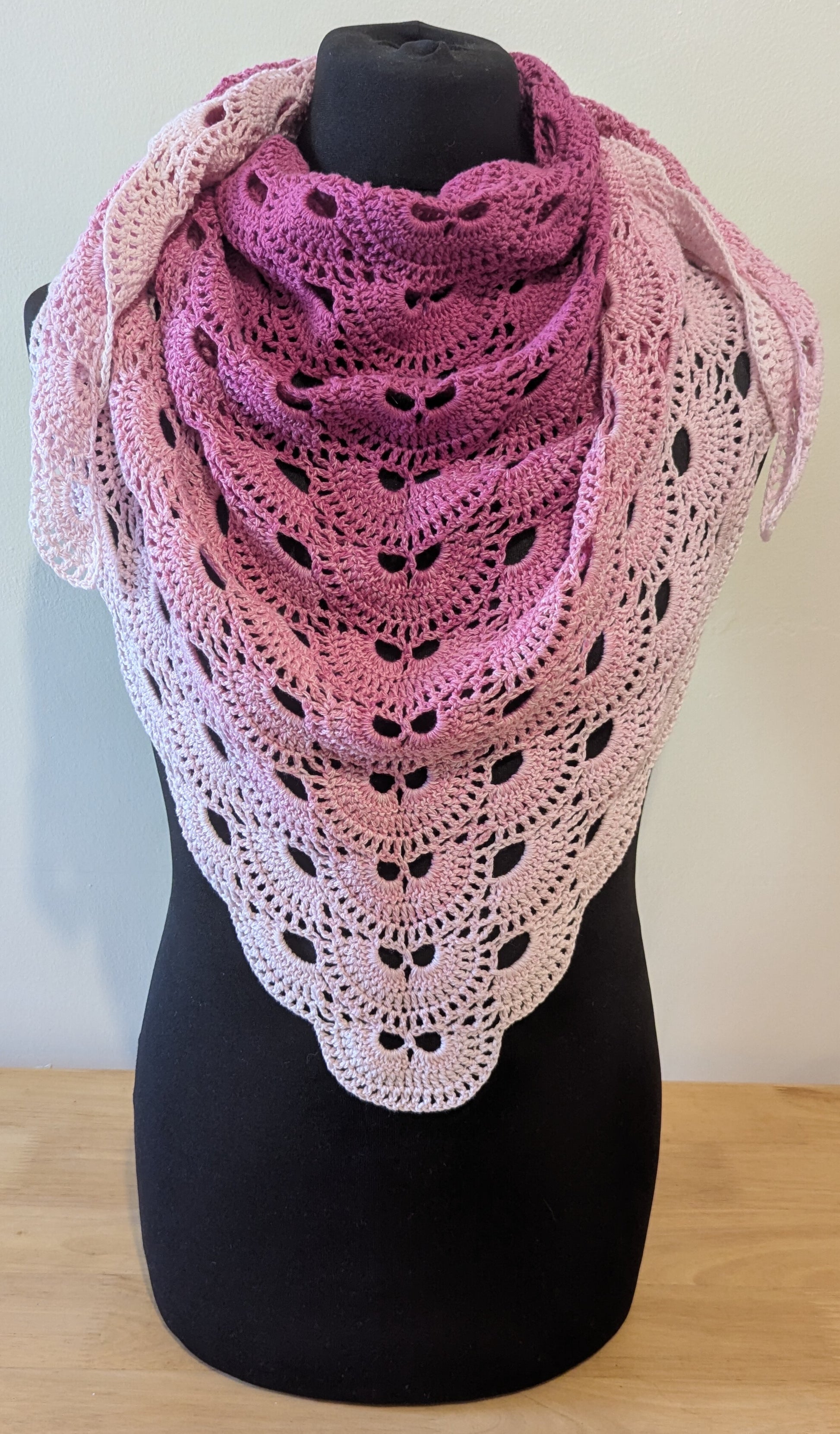 Crocheted shawl with a gradient of pink and white on a mannequin against a plain background