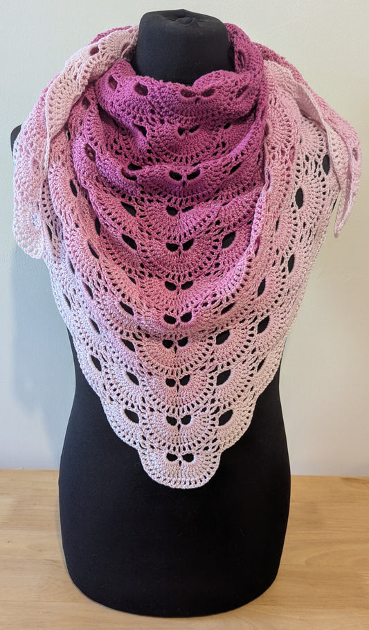 Crocheted shawl with a gradient of pink and white on a mannequin against a plain background