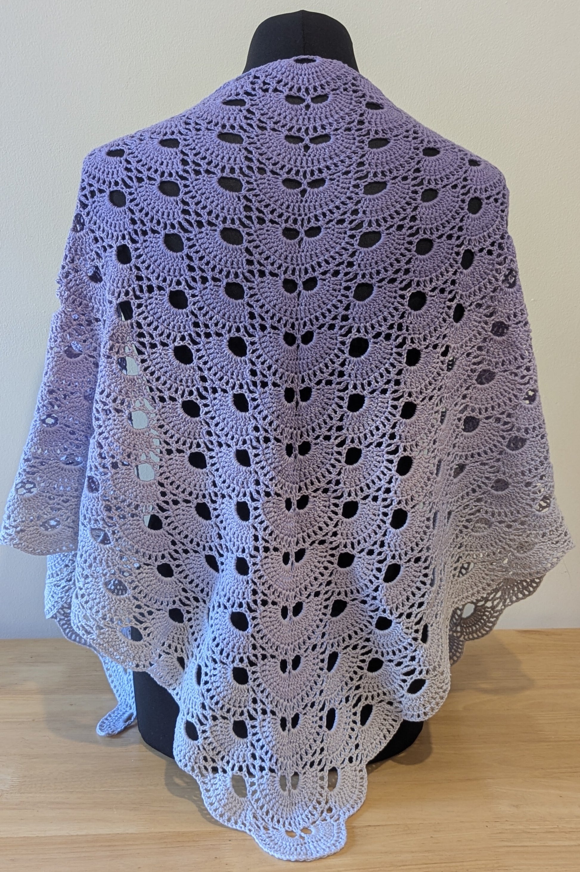 Crocheted shawl draped over a mannequin against a plain background