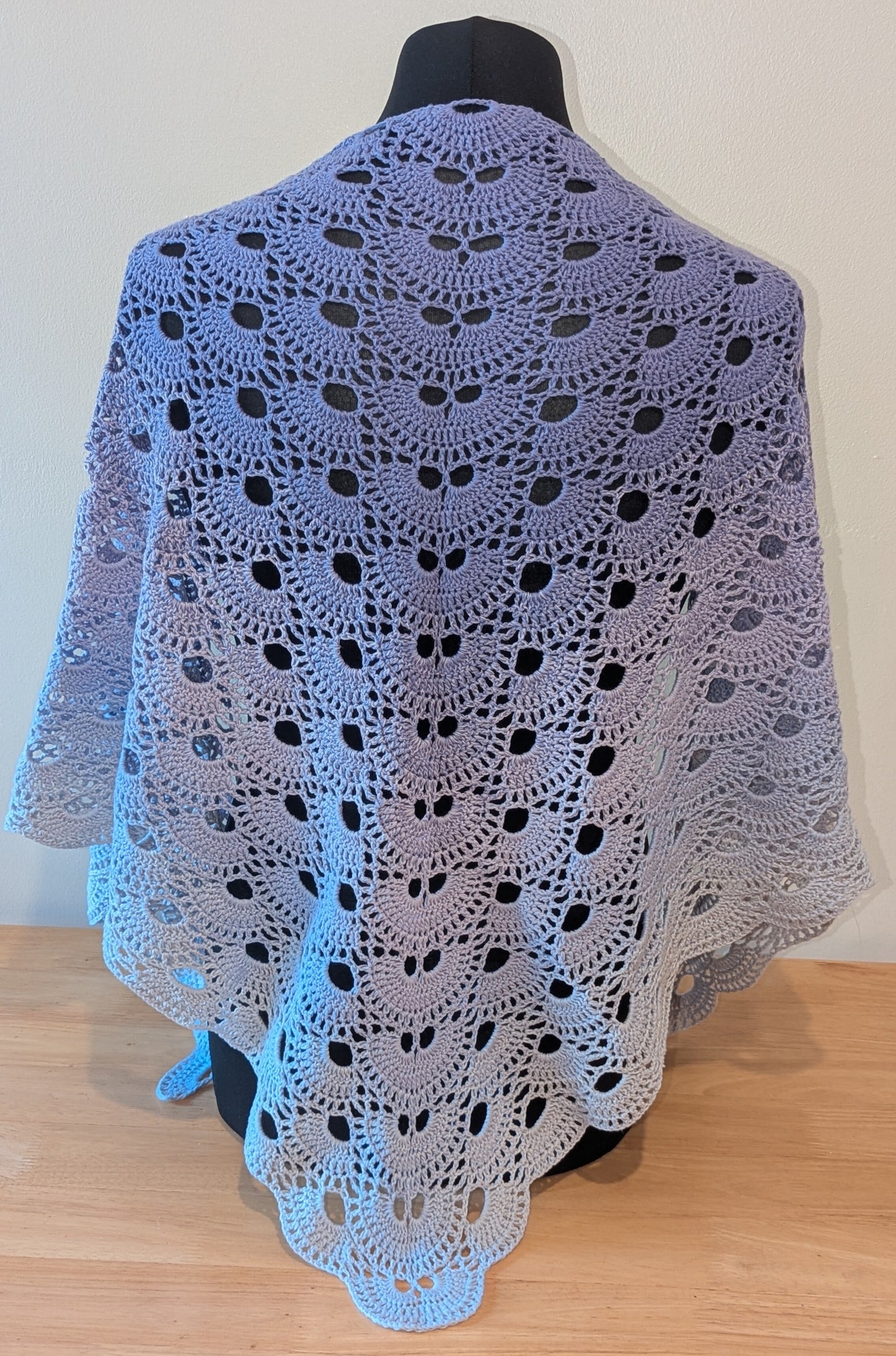 Crocheted shawl with a purple gradient draped over a mannequin against a plain background