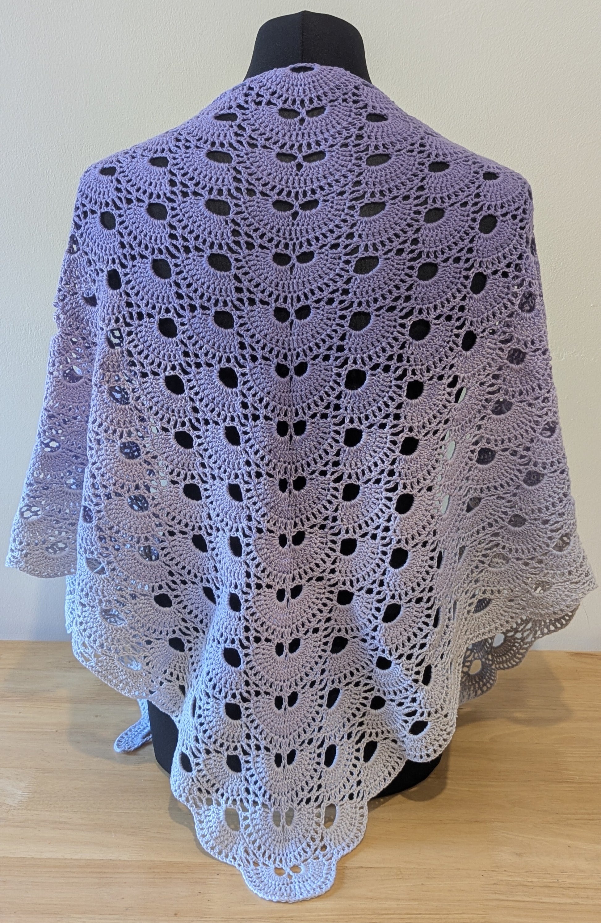 Crocheted shawl draped over a mannequin against a plain background