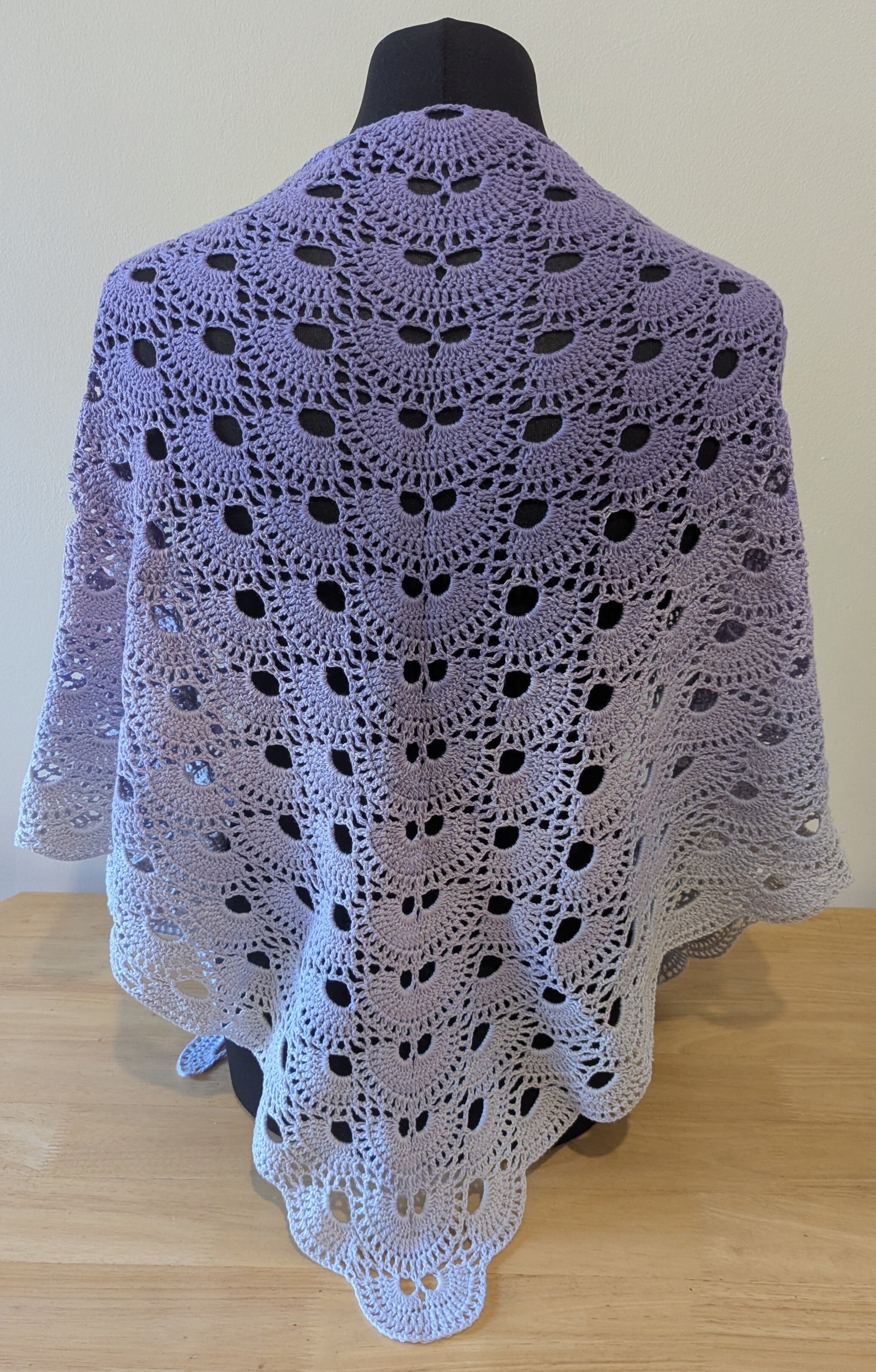 Crocheted shawl with a purple gradient draped over a mannequin against a plain background