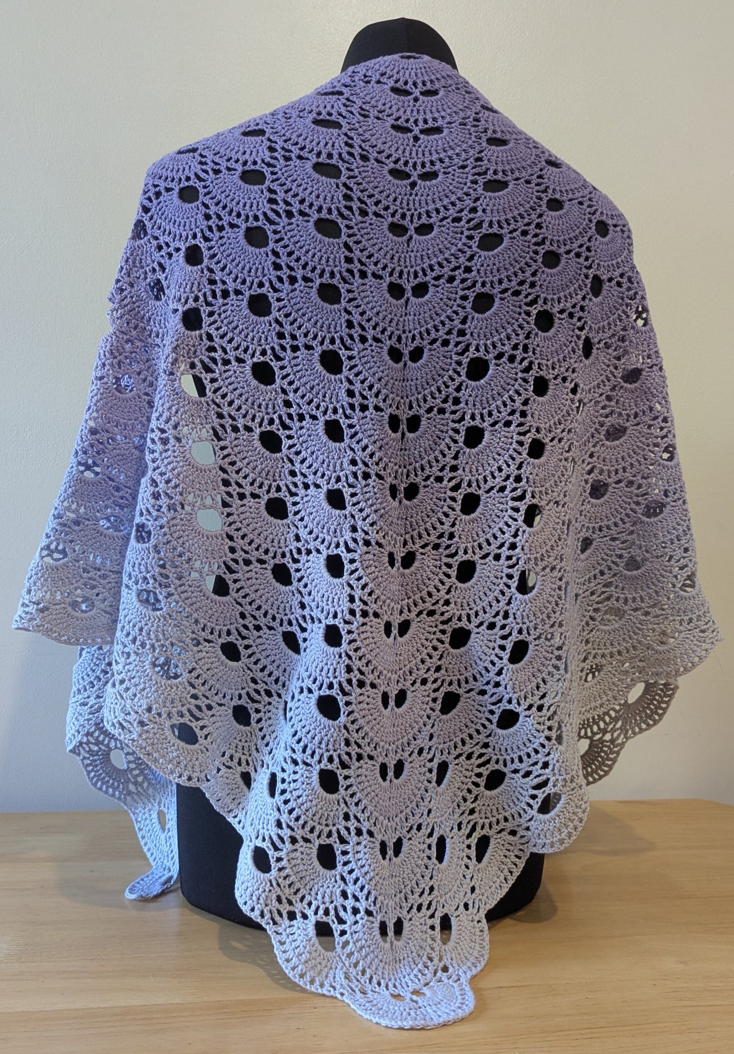 Crocheted shawl with a purple gradient draped over a mannequin against a plain background
