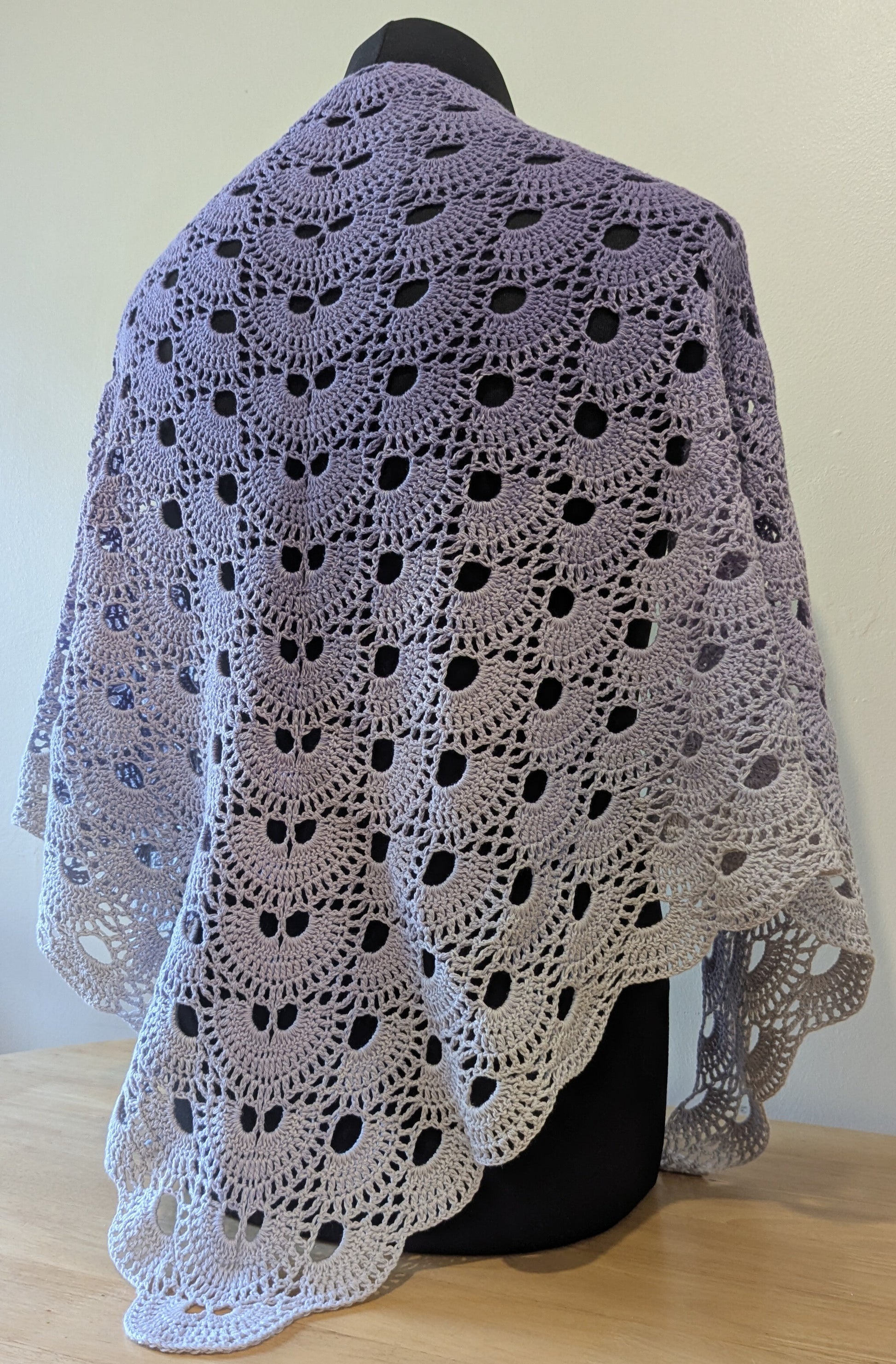 Crocheted shawl with a purple gradient draped over a mannequin against a plain background