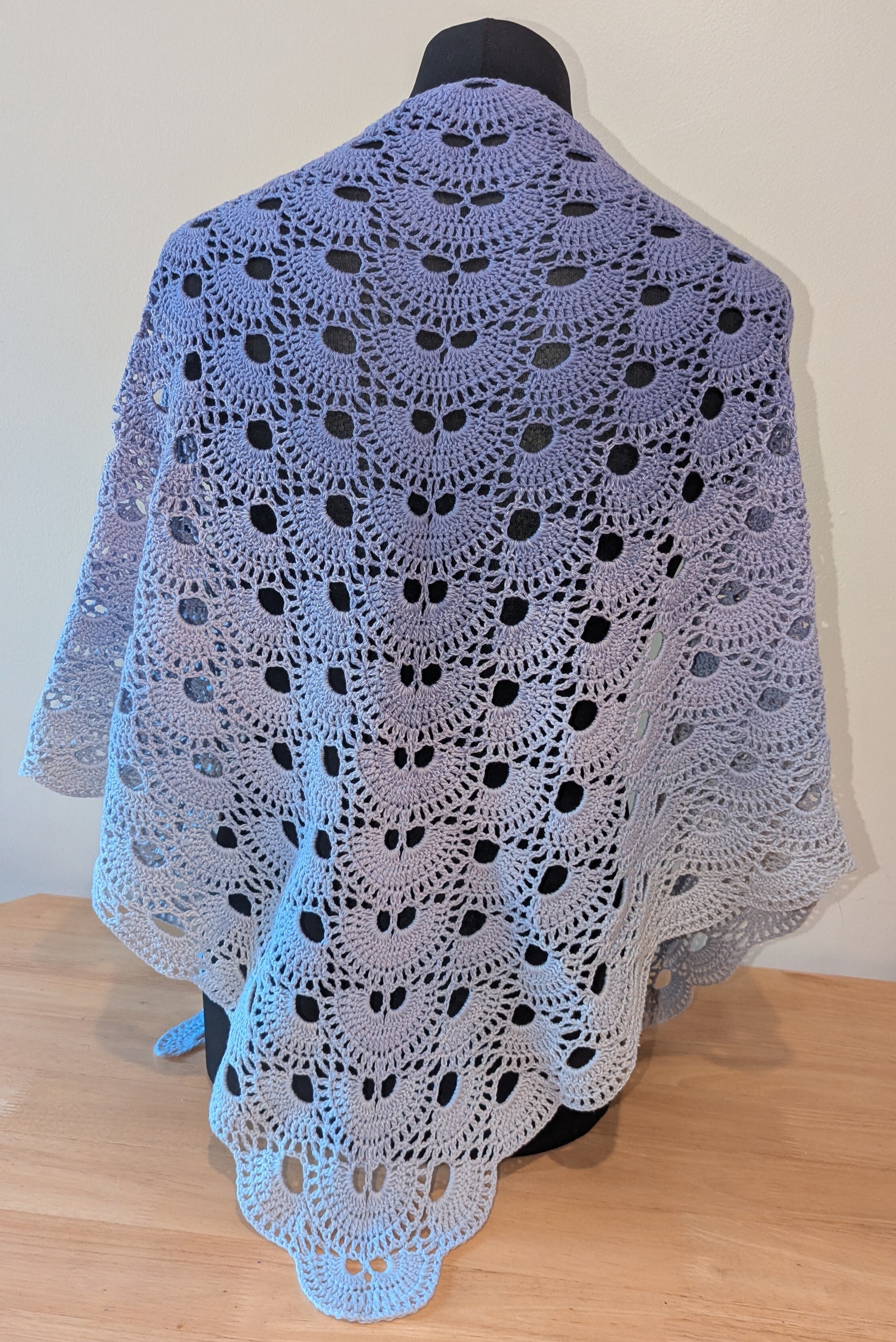 Crocheted shawl draped over a mannequin against a plain background