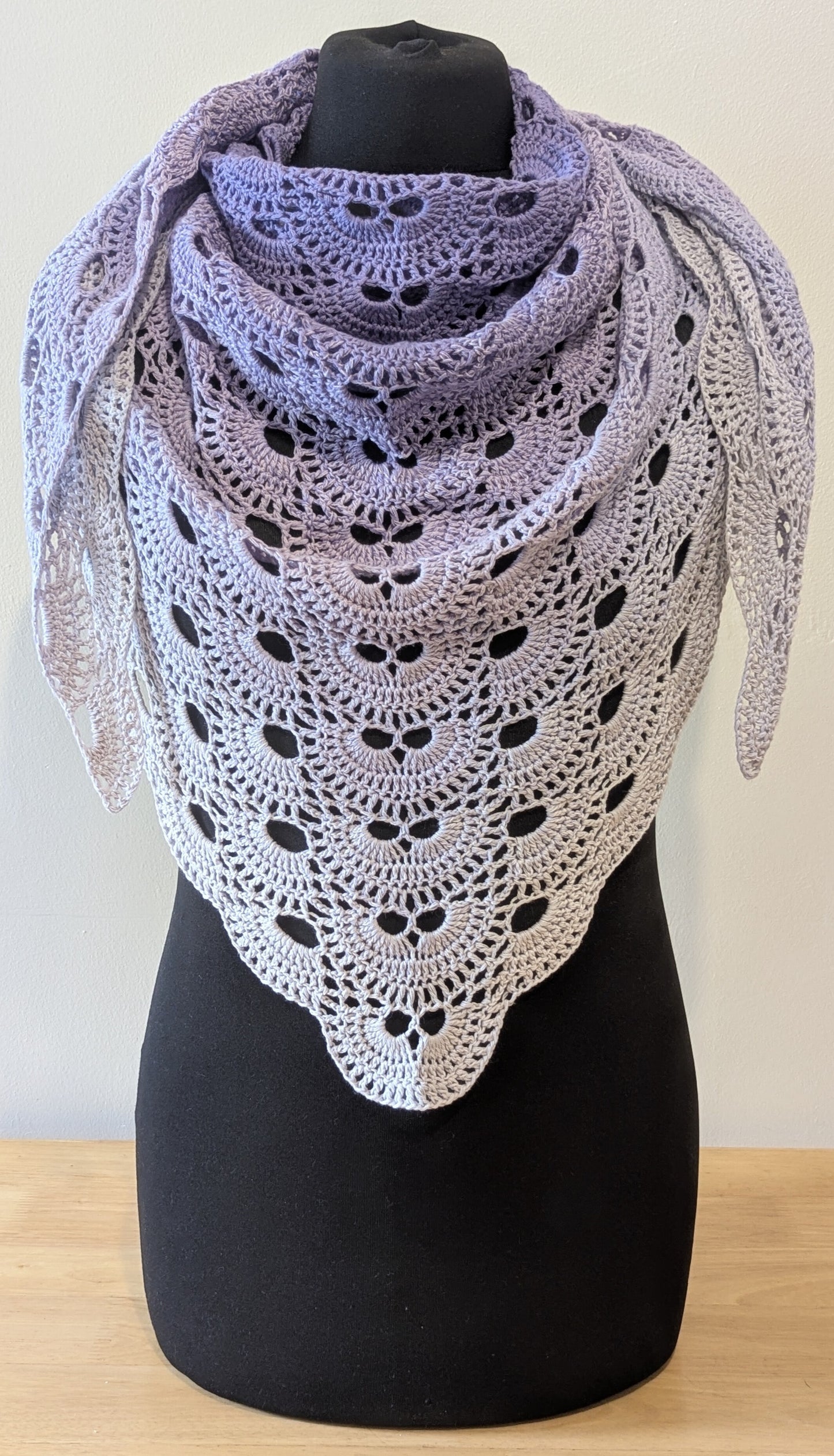 Crocheted shawl with a gradient from purple to white on a mannequin against a plain background