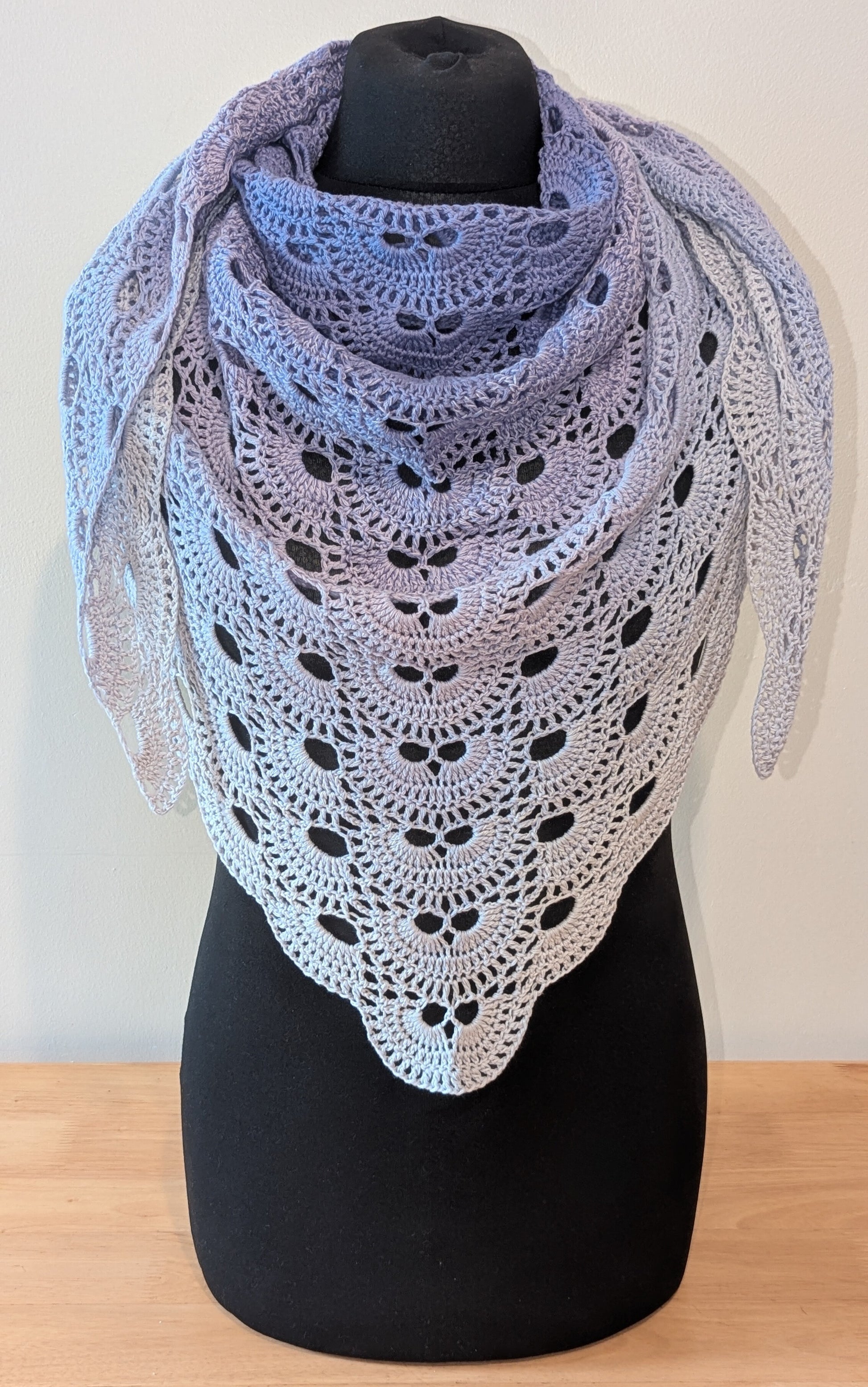 Crocheted shawl with a gradient of pastel purple on a black mannequin against a white background
