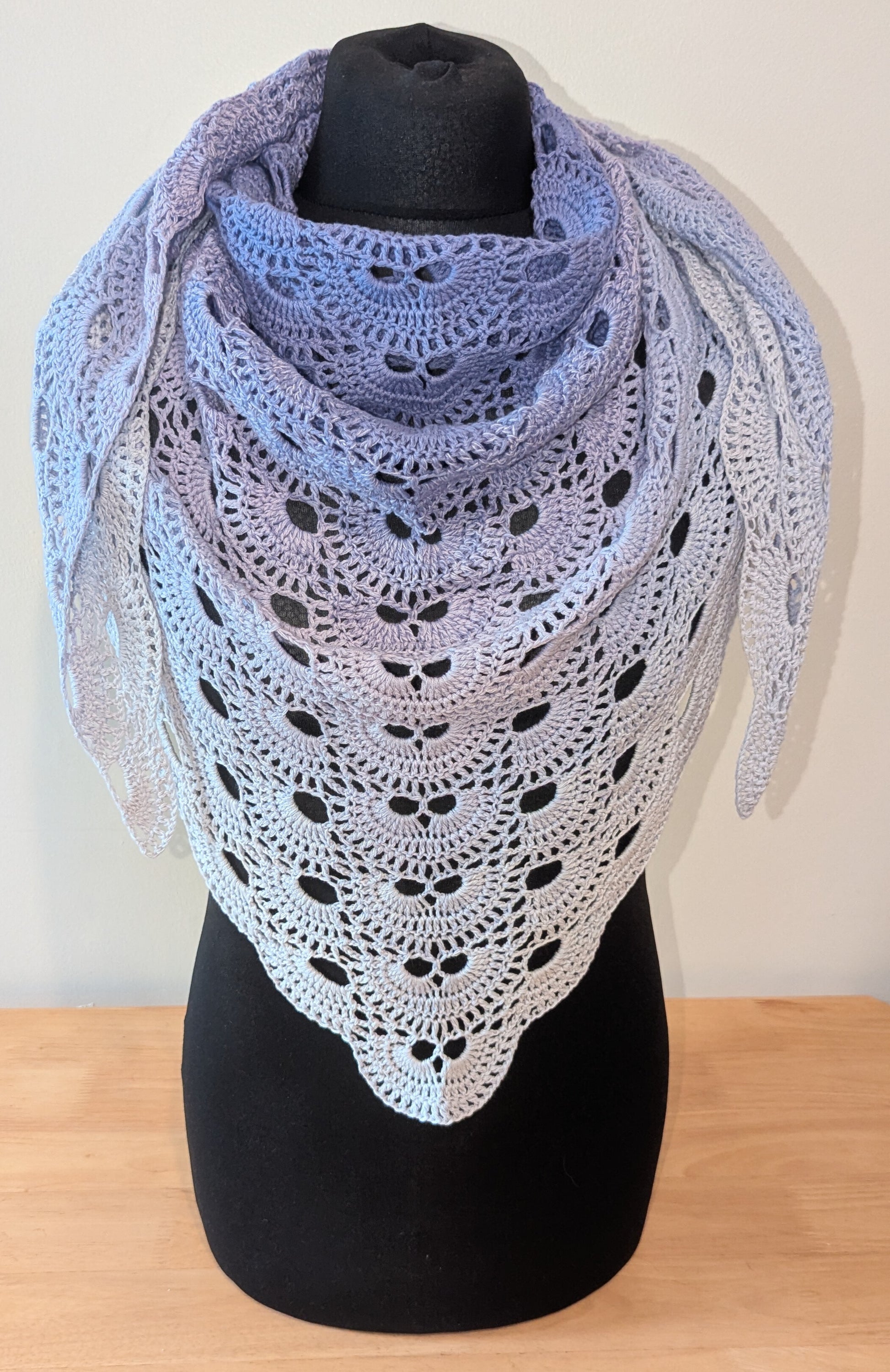 Crocheted shawl with a gradient of white and purple colors on a black mannequin against a white background.