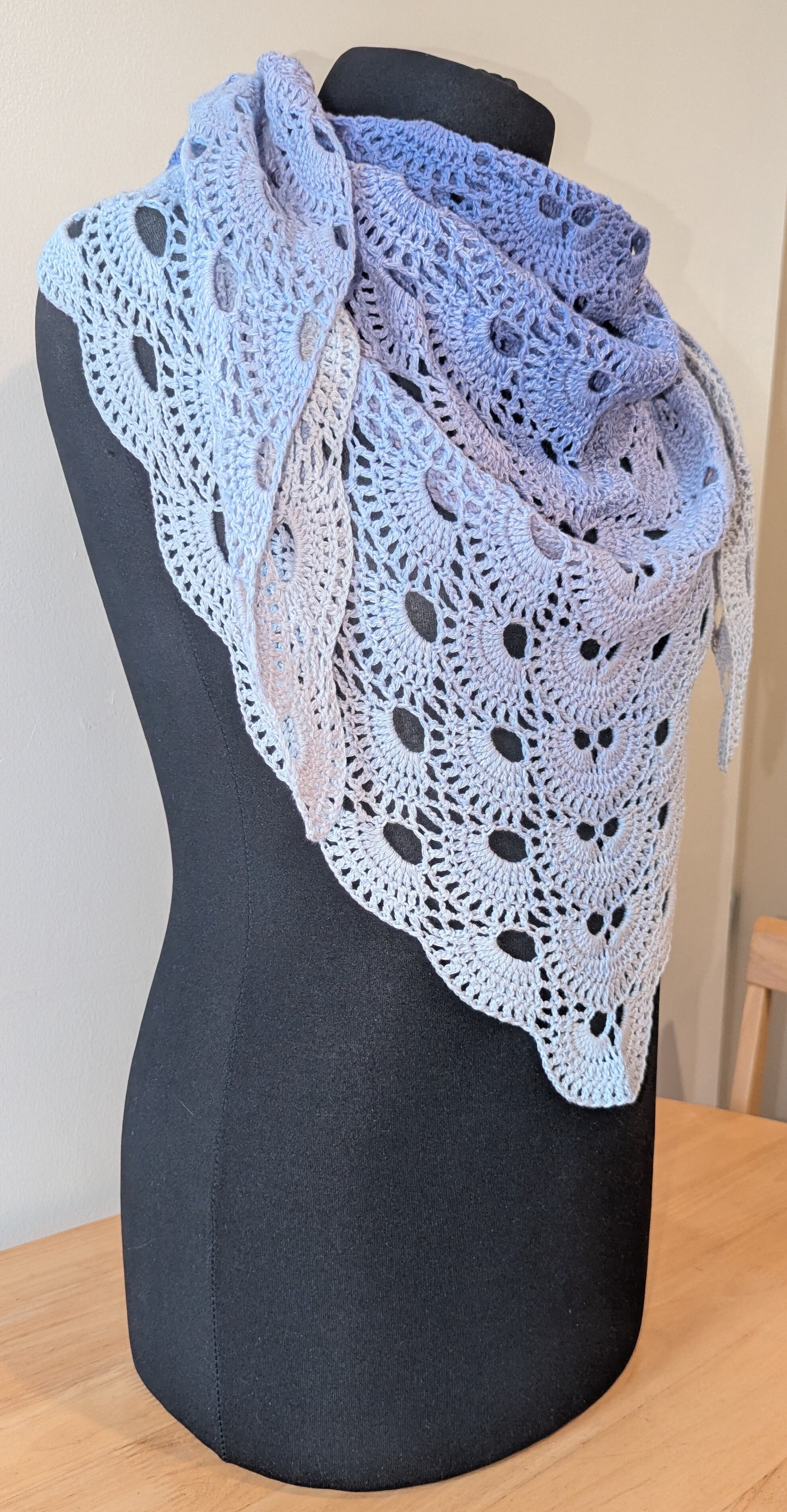 Crocheted shawl with a lace pattern draped over a mannequin against a neutral background