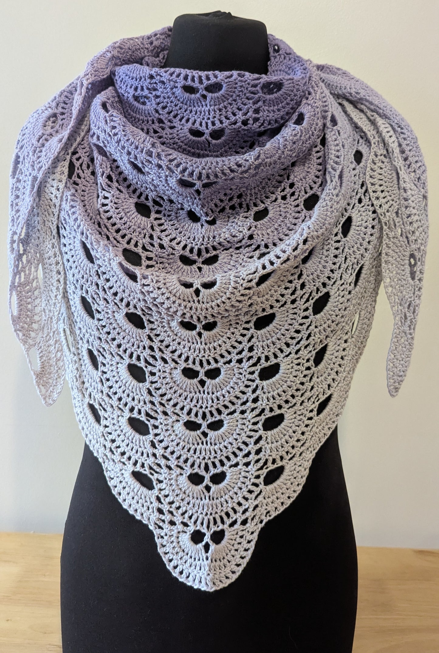 Crocheted shawl with a lacey gradient on a mannequin against a plain background