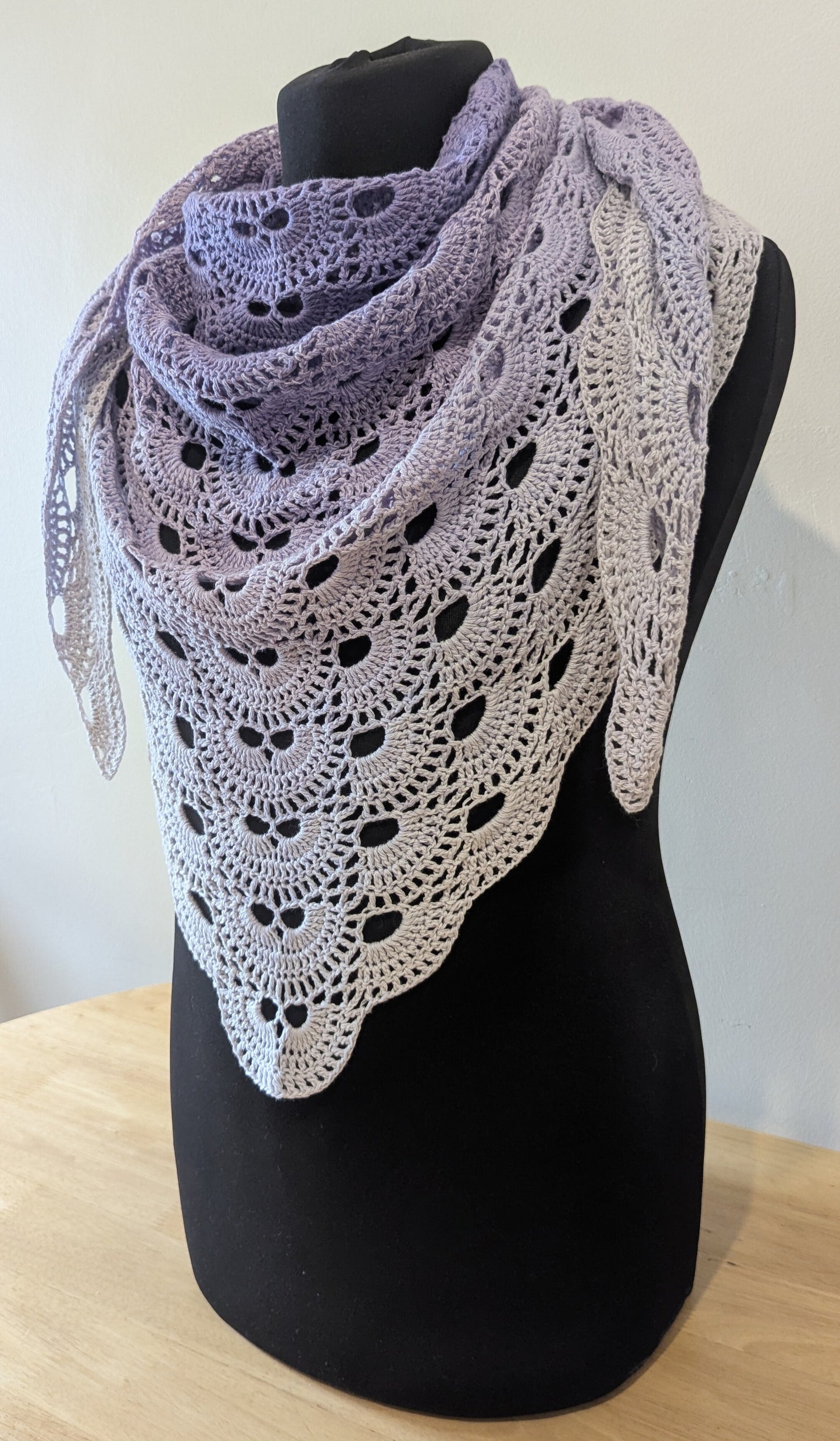 Crocheted shawl with a gradient from purple to white on a black mannequin against a neutral background.