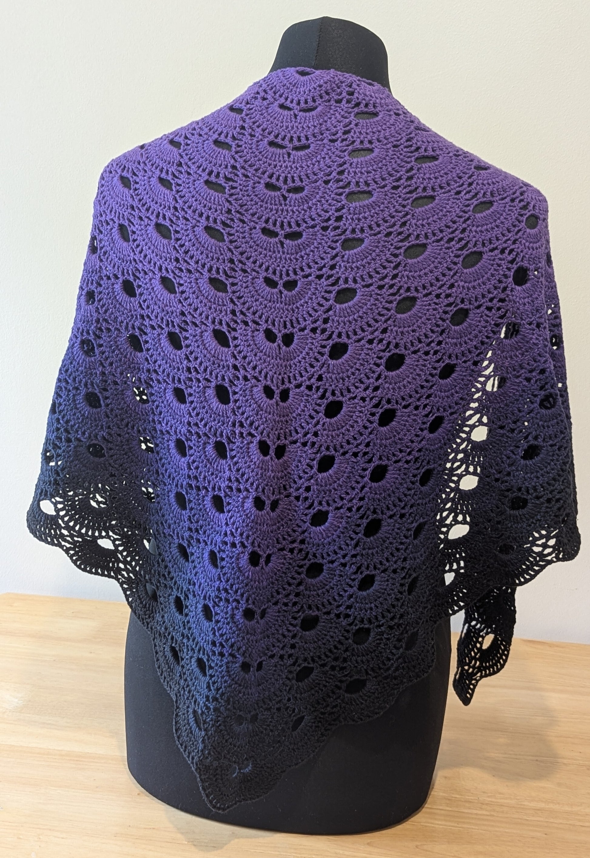 Purple crocheted shawl on a mannequin against a white background