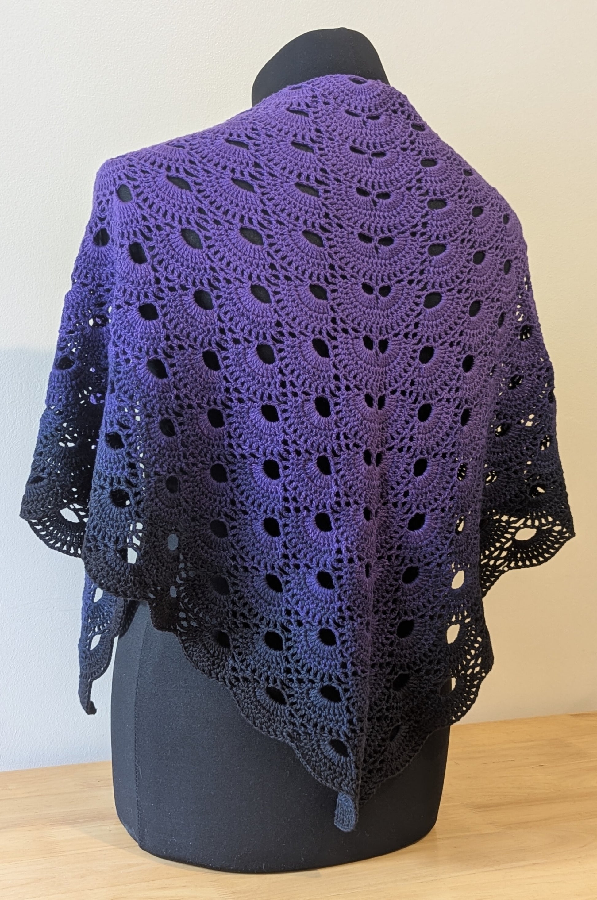 Purple crocheted shawl on a mannequin against a plain background