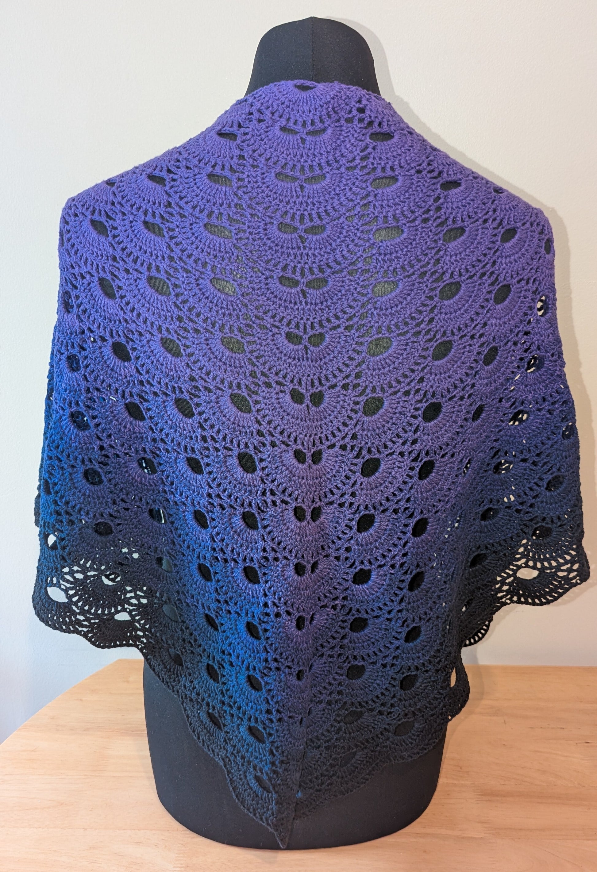 Purple crocheted shawl on a mannequin against a white background