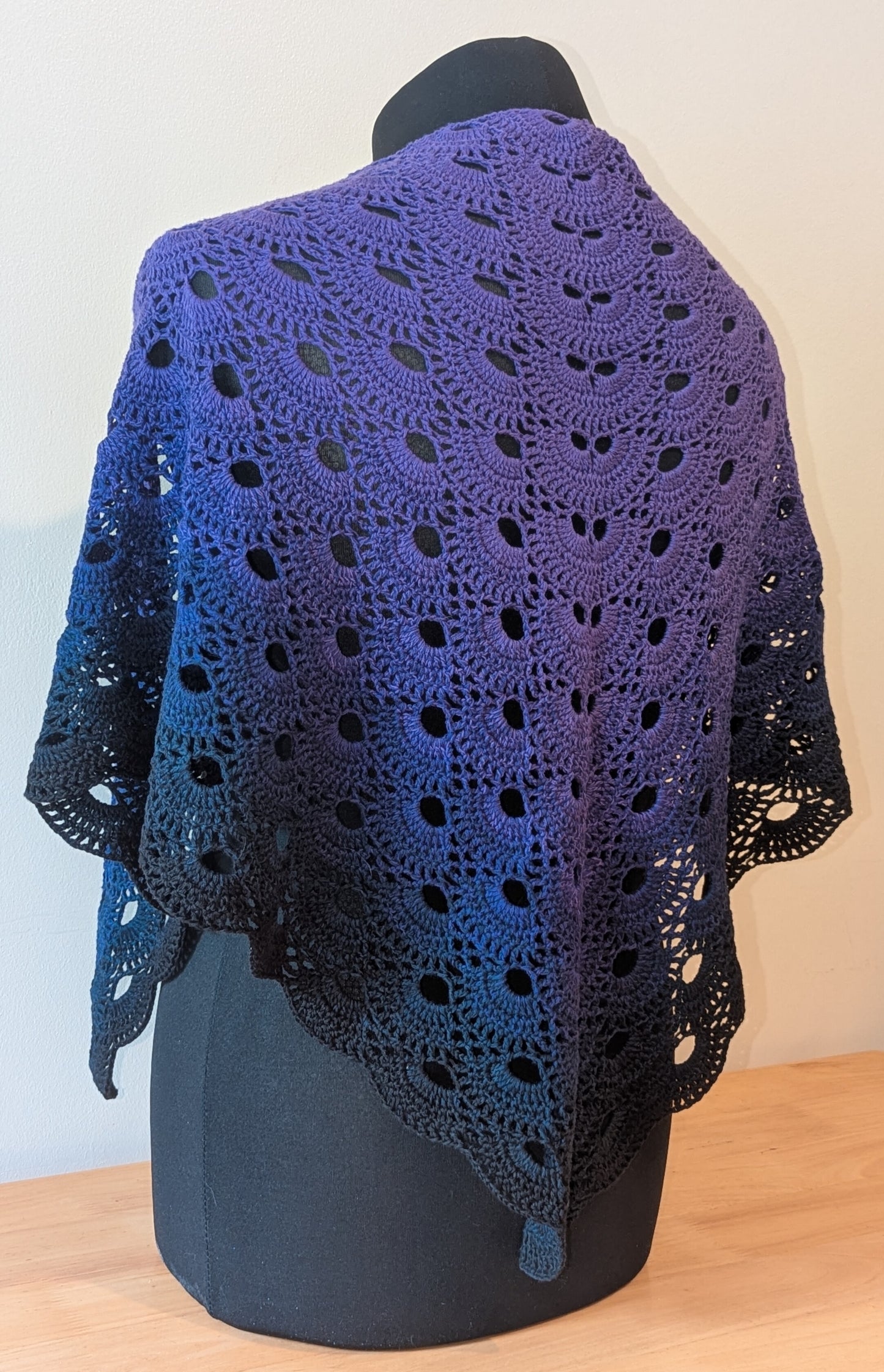 Purple and black crocheted shawl on a mannequin against a light background