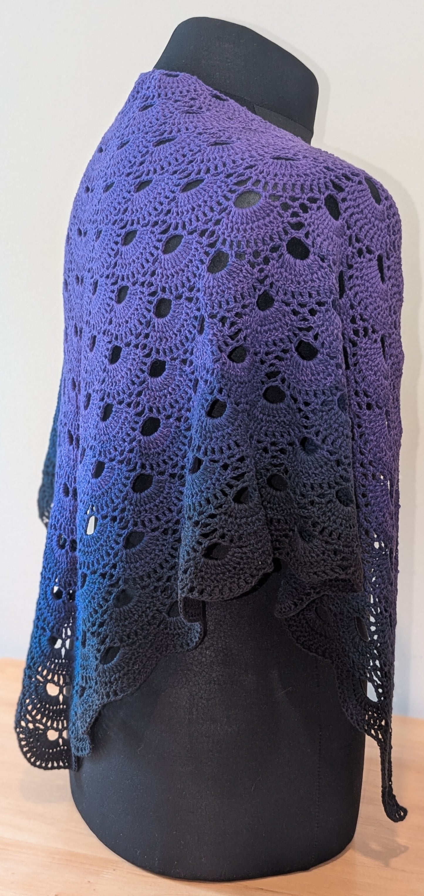 Purple crochet shawl on a mannequin against a white background