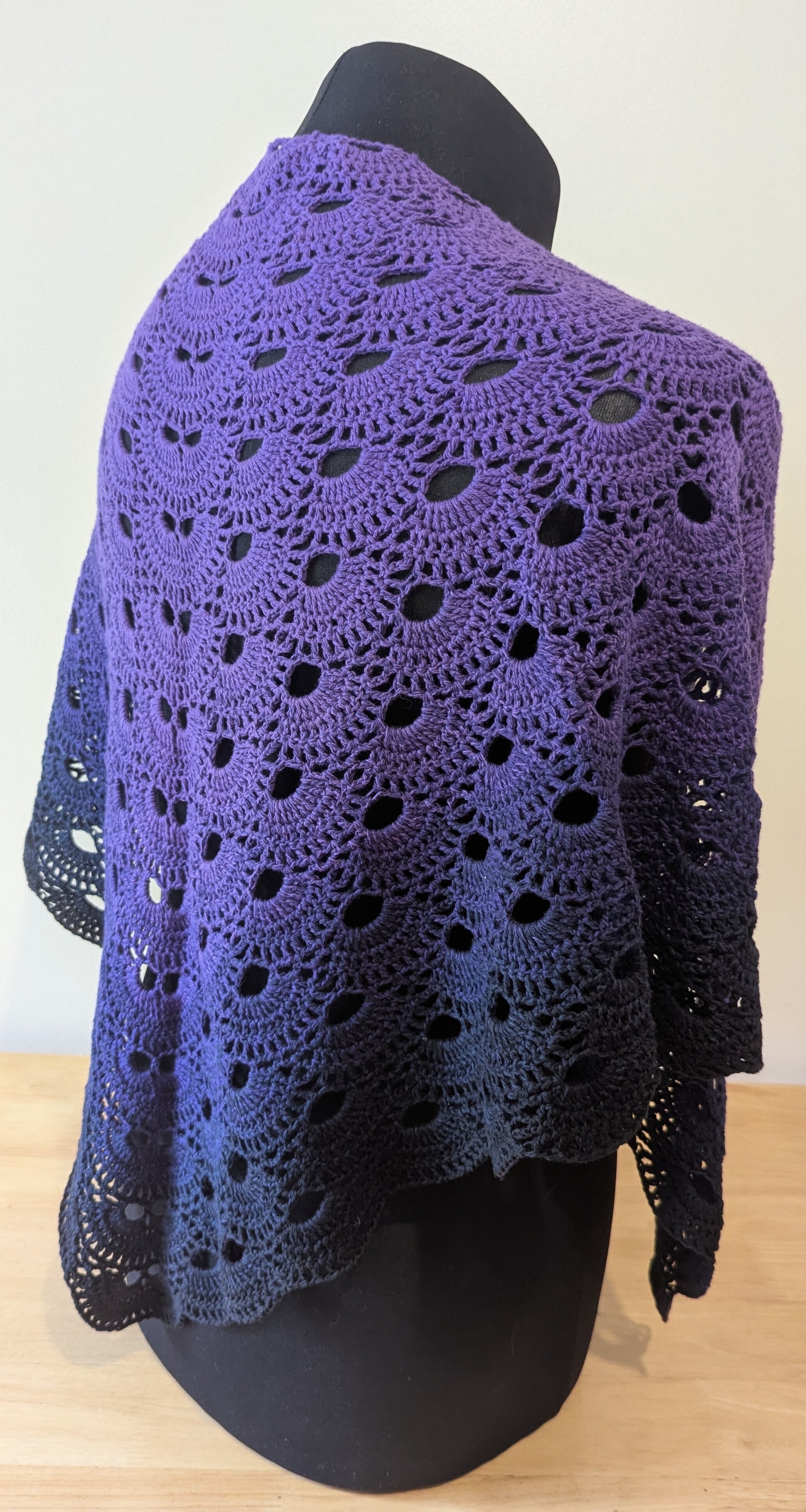 Purple crocheted shawl on a mannequin against a white background