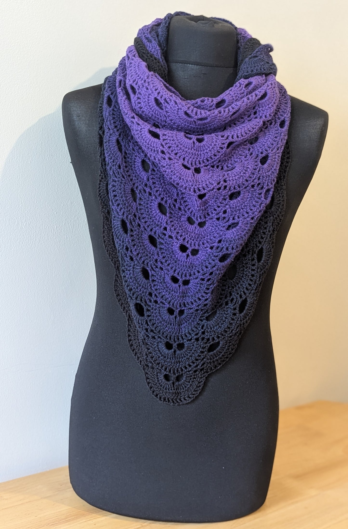 Purple crocheted shawl on a black mannequin against a beige background