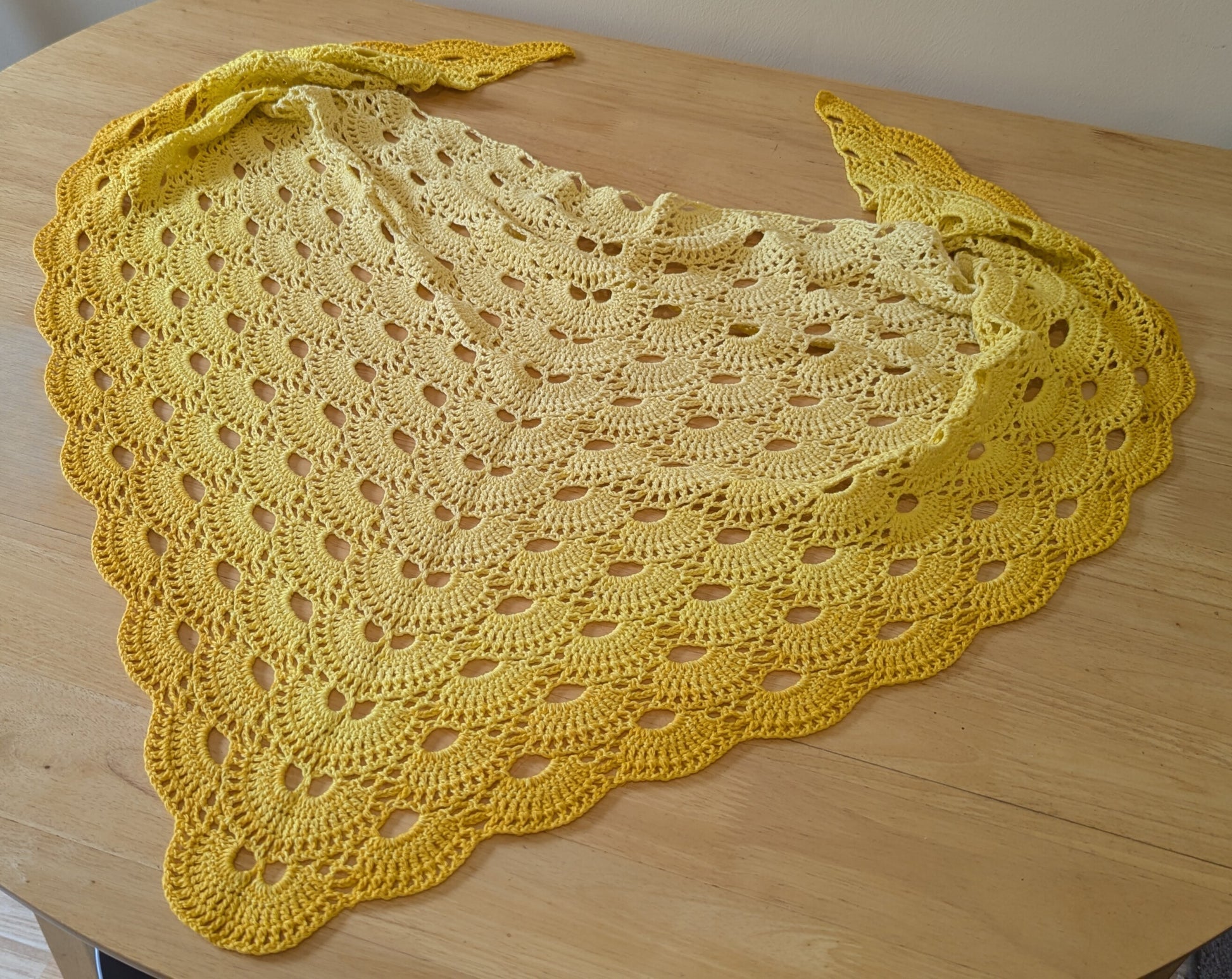 Yellow crocheted shawl on a wooden surface