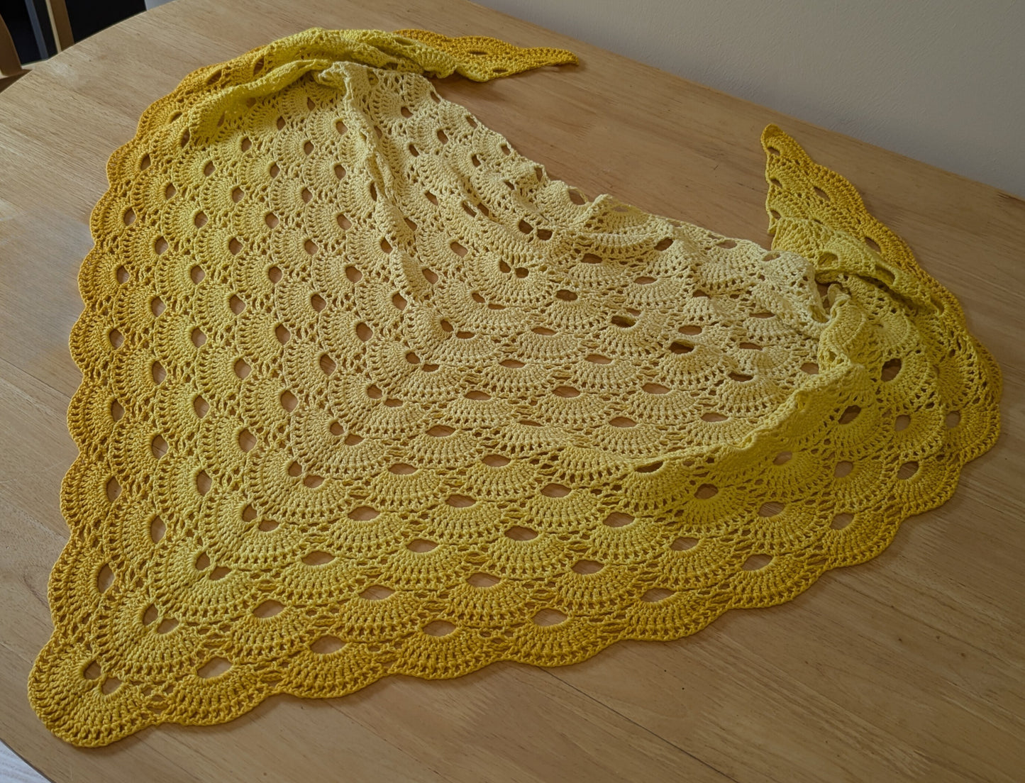 Yellow crocheted shawl on a wooden surface