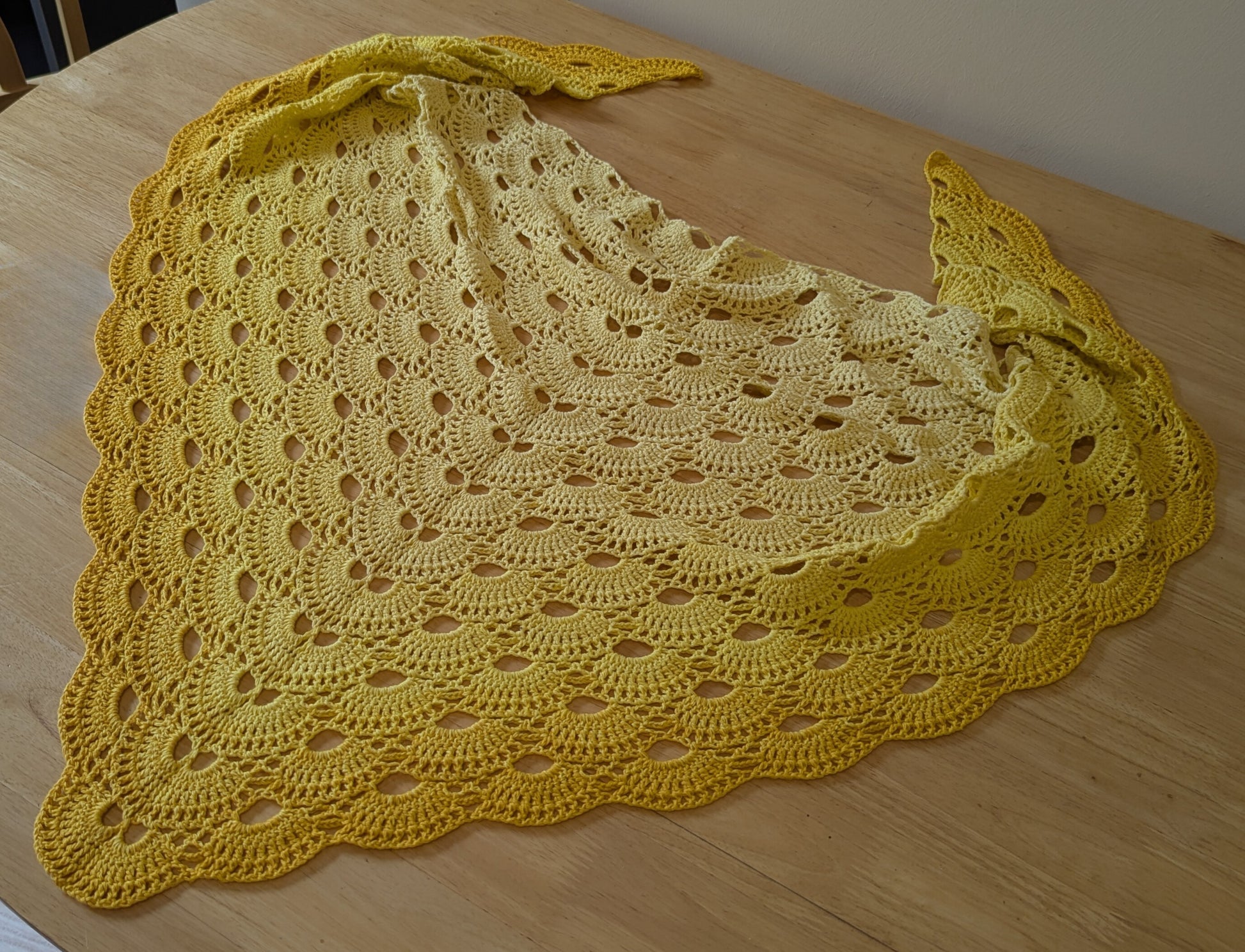 Yellow crocheted shawl on a wooden surface