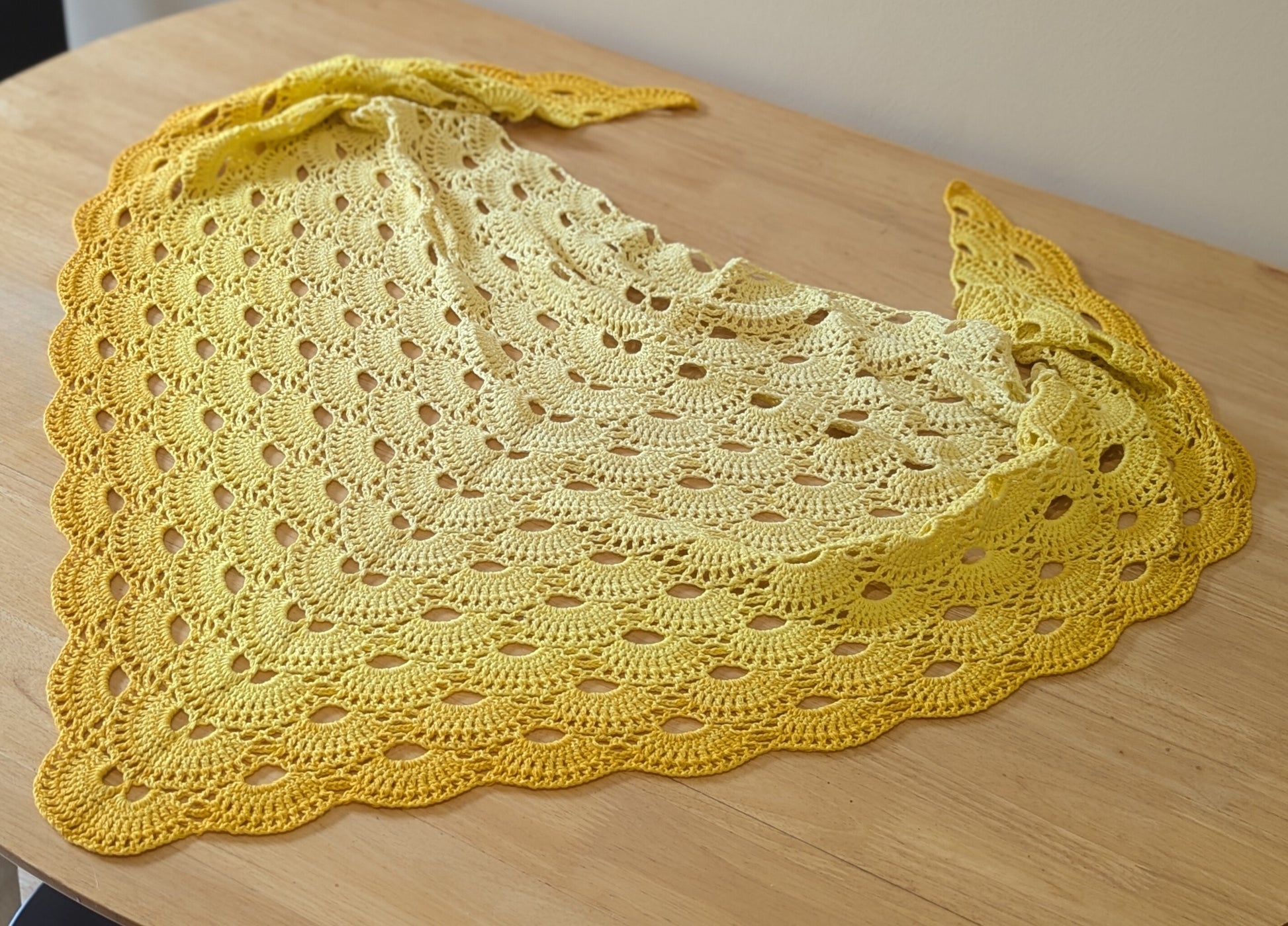 Yellow crocheted shawl on a wooden surface