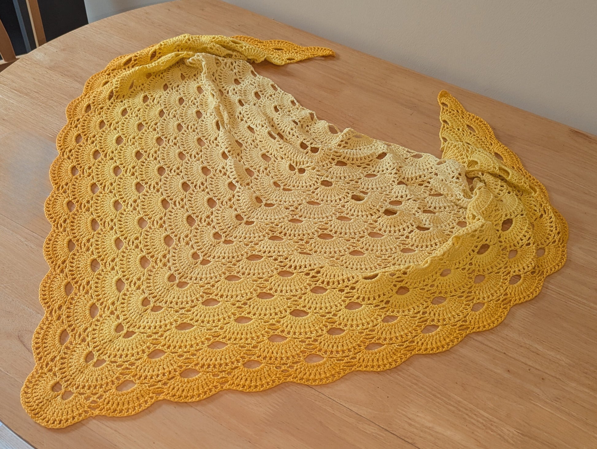 Yellow crocheted shawl on a wooden surface