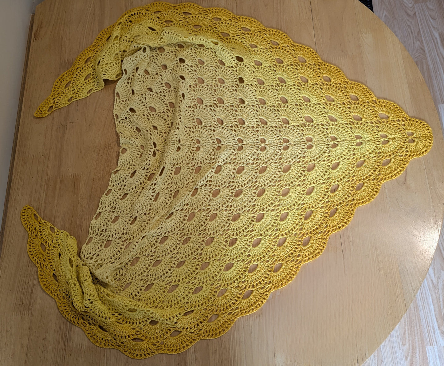 Yellow crocheted shawl on a wooden surface