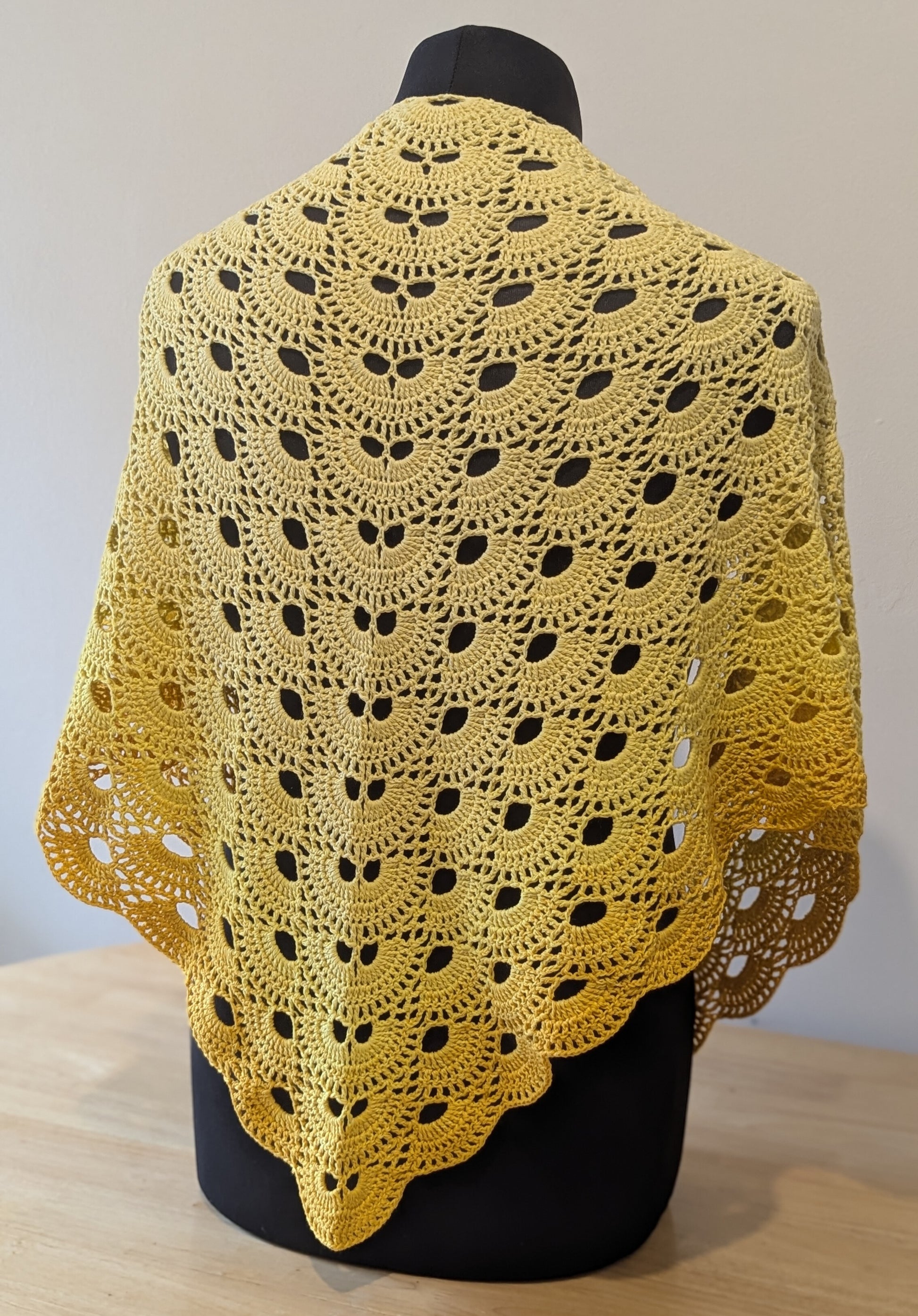 Yellow crocheted shawl on a mannequin against a plain background