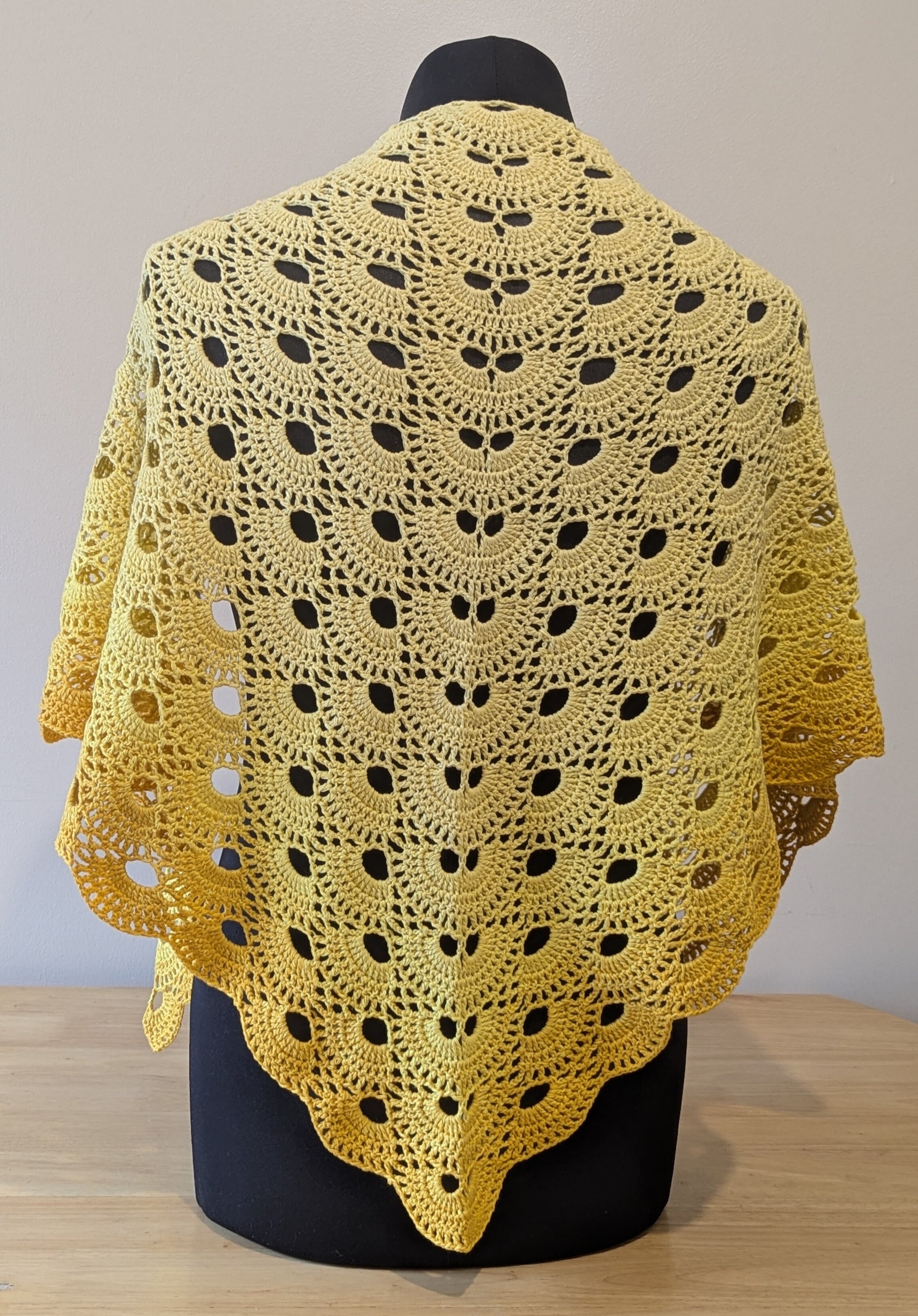 Yellow crocheted shawl on a mannequin against a plain background