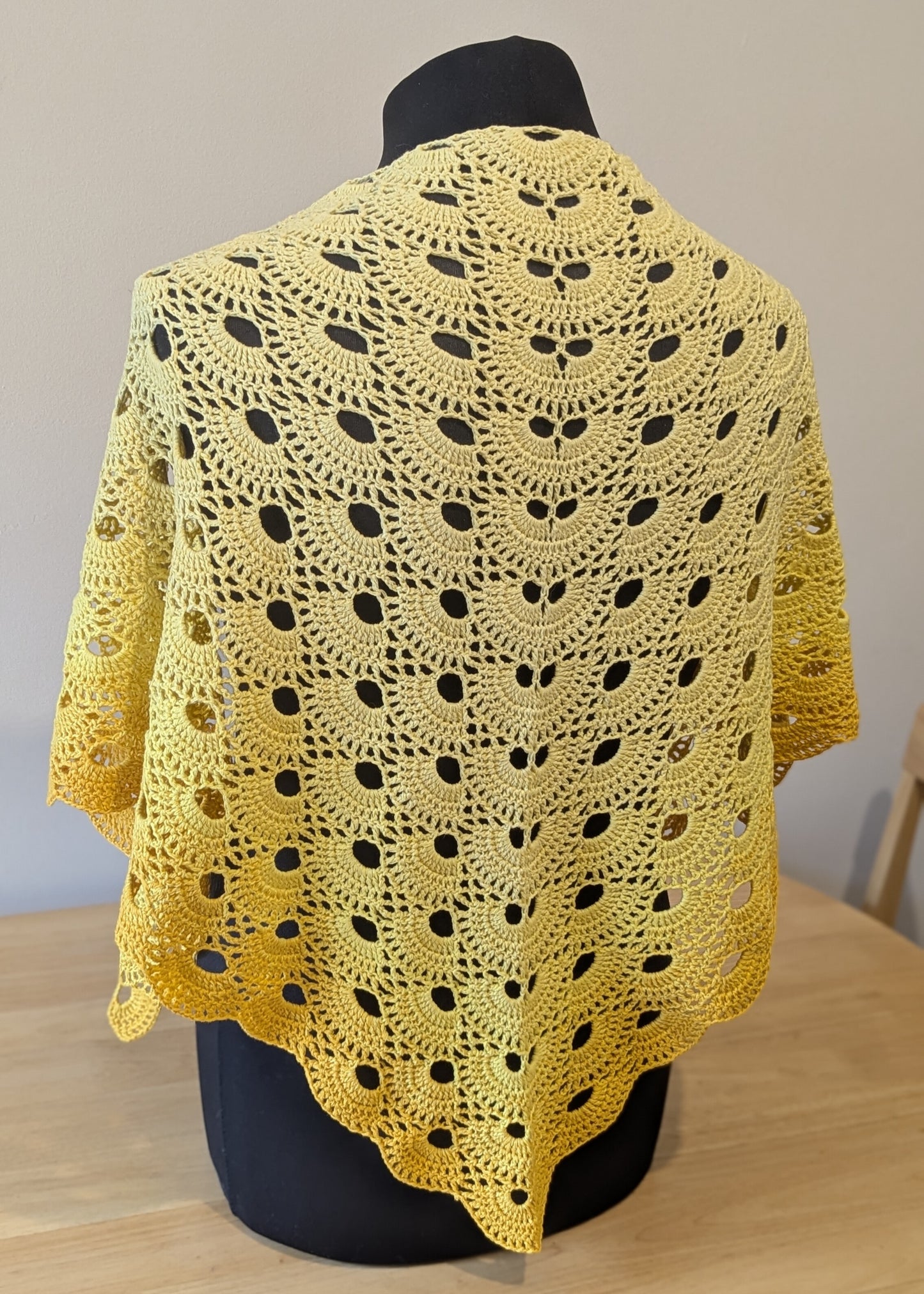 Yellow crocheted shawl on a mannequin against a neutral background