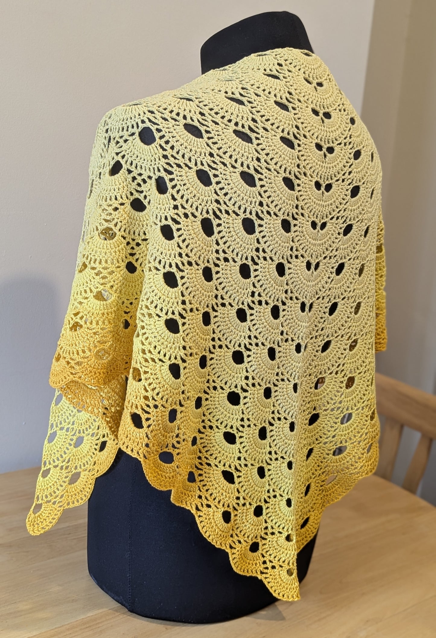 Yellow crocheted shawl on a mannequin against a neutral background