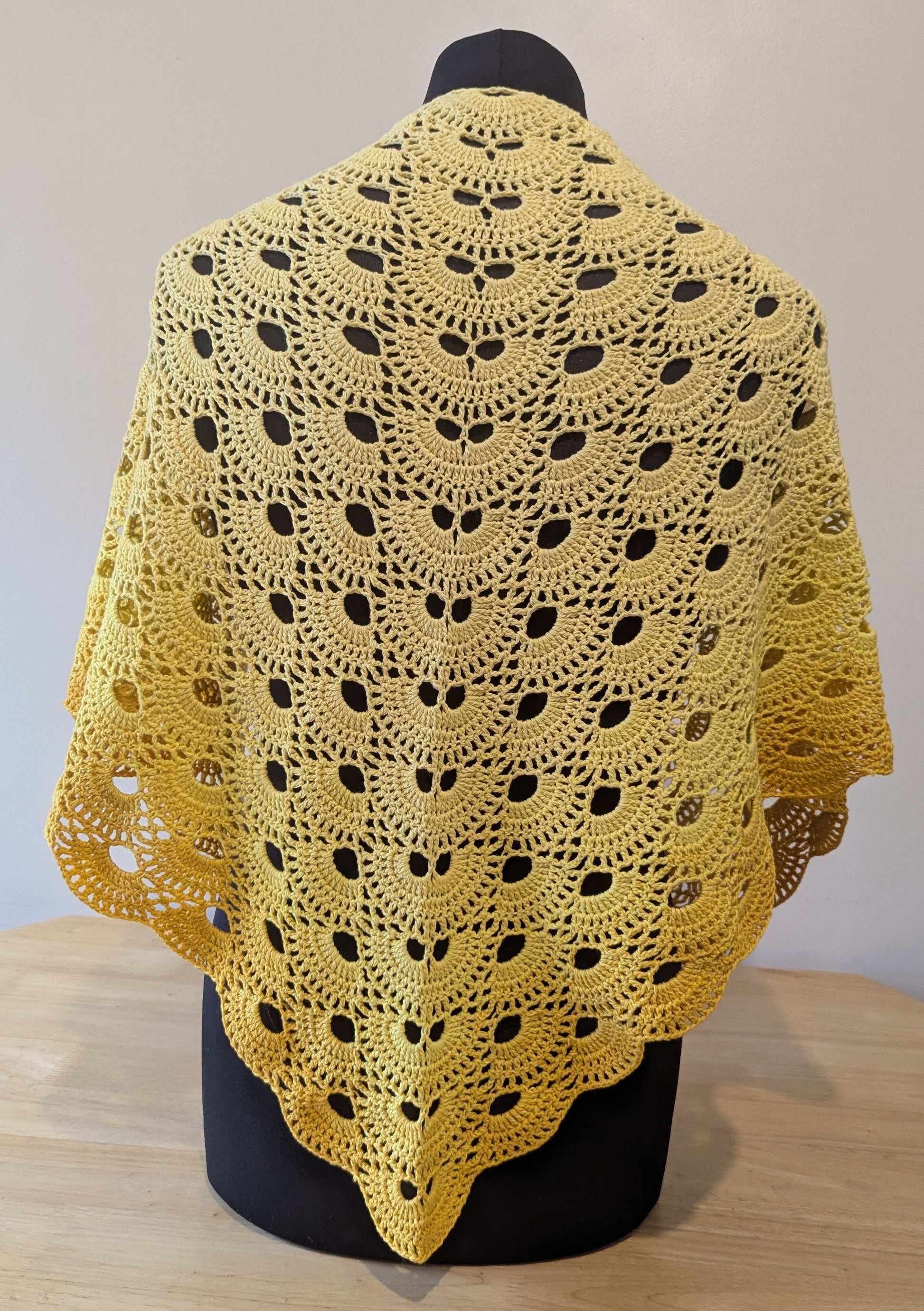 Yellow crocheted shawl on a mannequin against a plain background