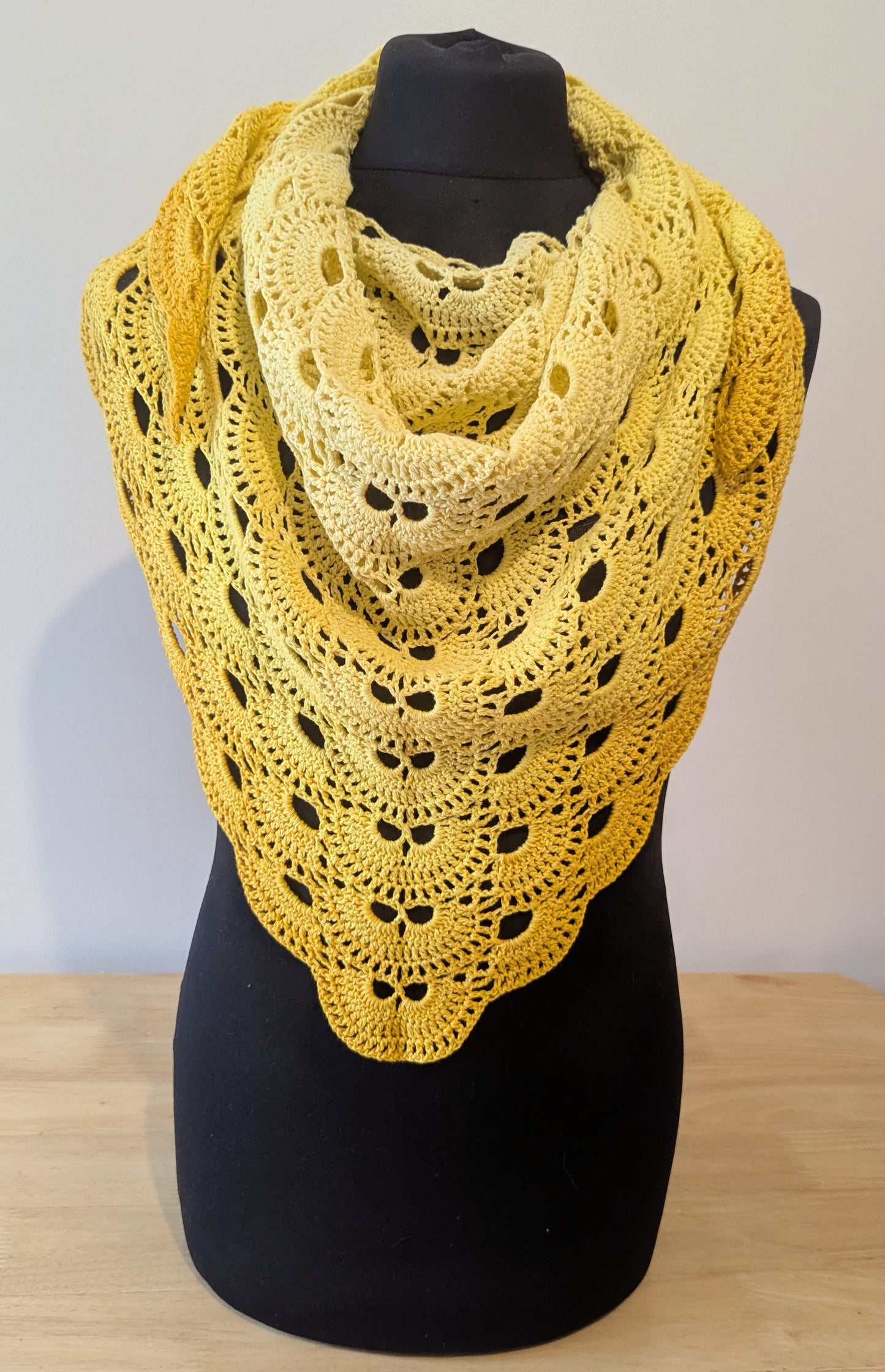 Yellow crochet shawl on a black mannequin against a plain background